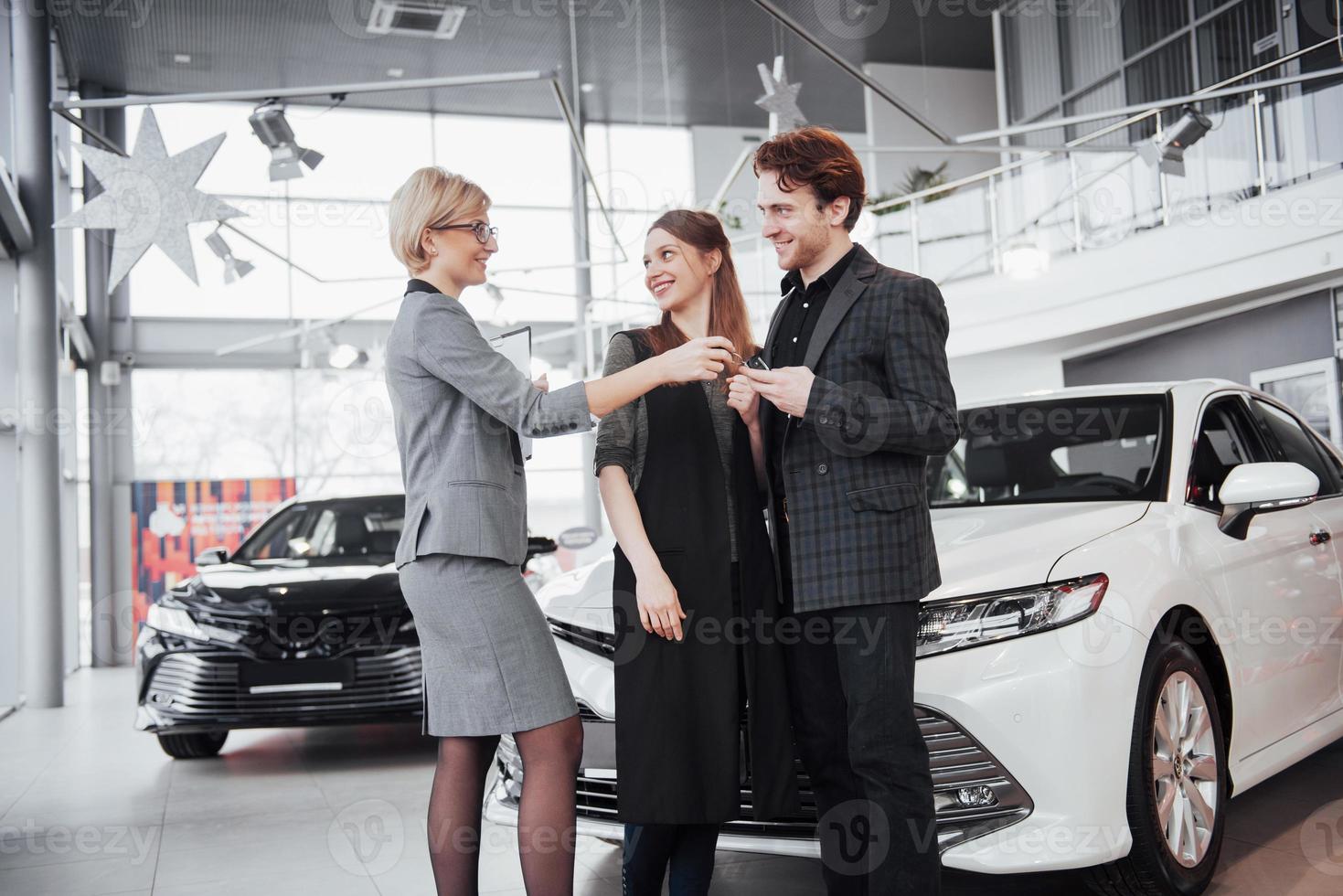 jetzt wird ihr traum wahr. Autoverkäufer, der den jungen attraktiven Besitzern den Schlüssel des neuen Autos übergibt foto