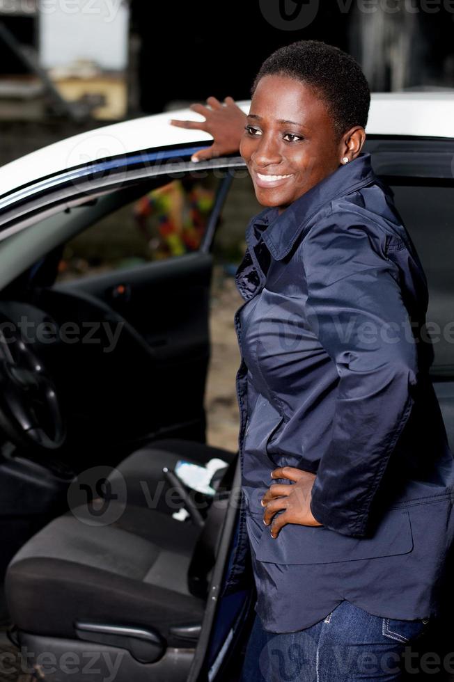 lächelnde Mechaniker der jungen Frau, die neben einem Auto steht. foto