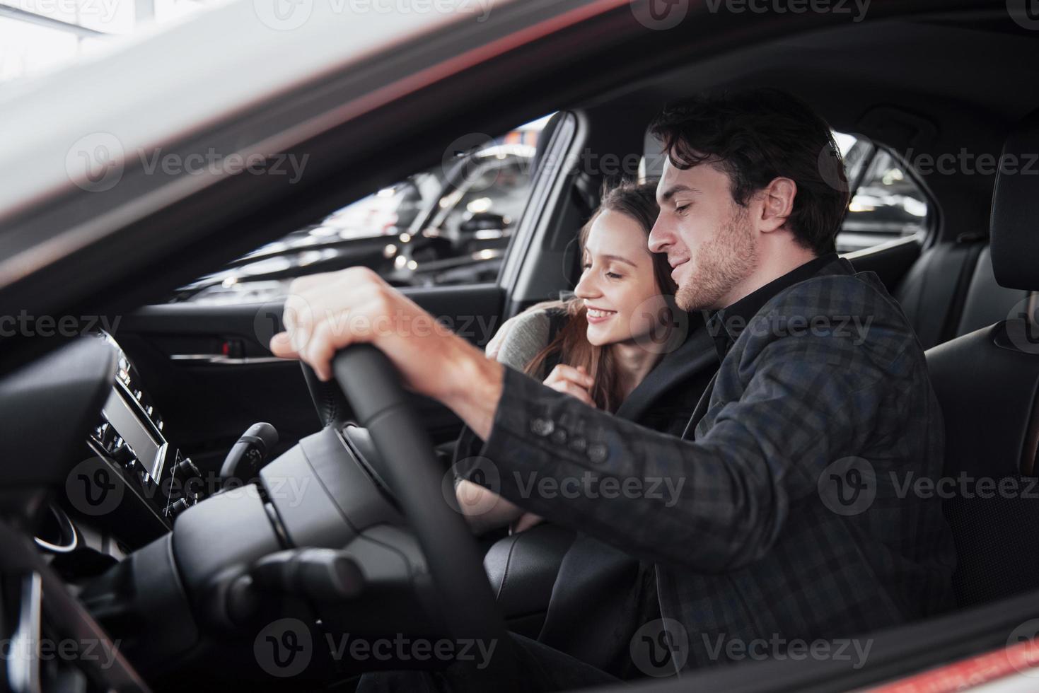 ihre Entscheidung treffen. Schönes Liebespaar, das zusammen in einem neuen Auto im Autohaus sitzt, gutaussehender Mann und seine liebevolle Freundin, die ein Auto zusammen mit einem Konsumfahrzeug auswählen foto