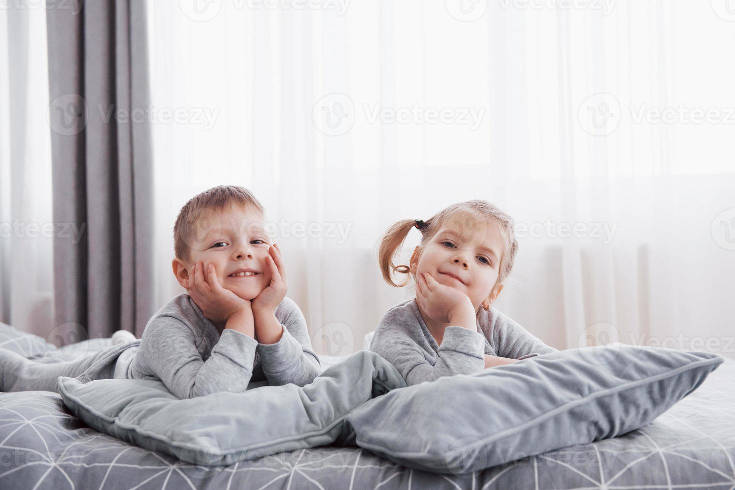 glückliche Kinder, die im weißen Schlafzimmer spielen. kleiner Junge und Mädchen, Bruder und Schwester spielen im Schlafanzug auf dem Bett. Nachtwäsche und Bettwäsche für Babys und Kleinkinder. Familie zu Hause foto