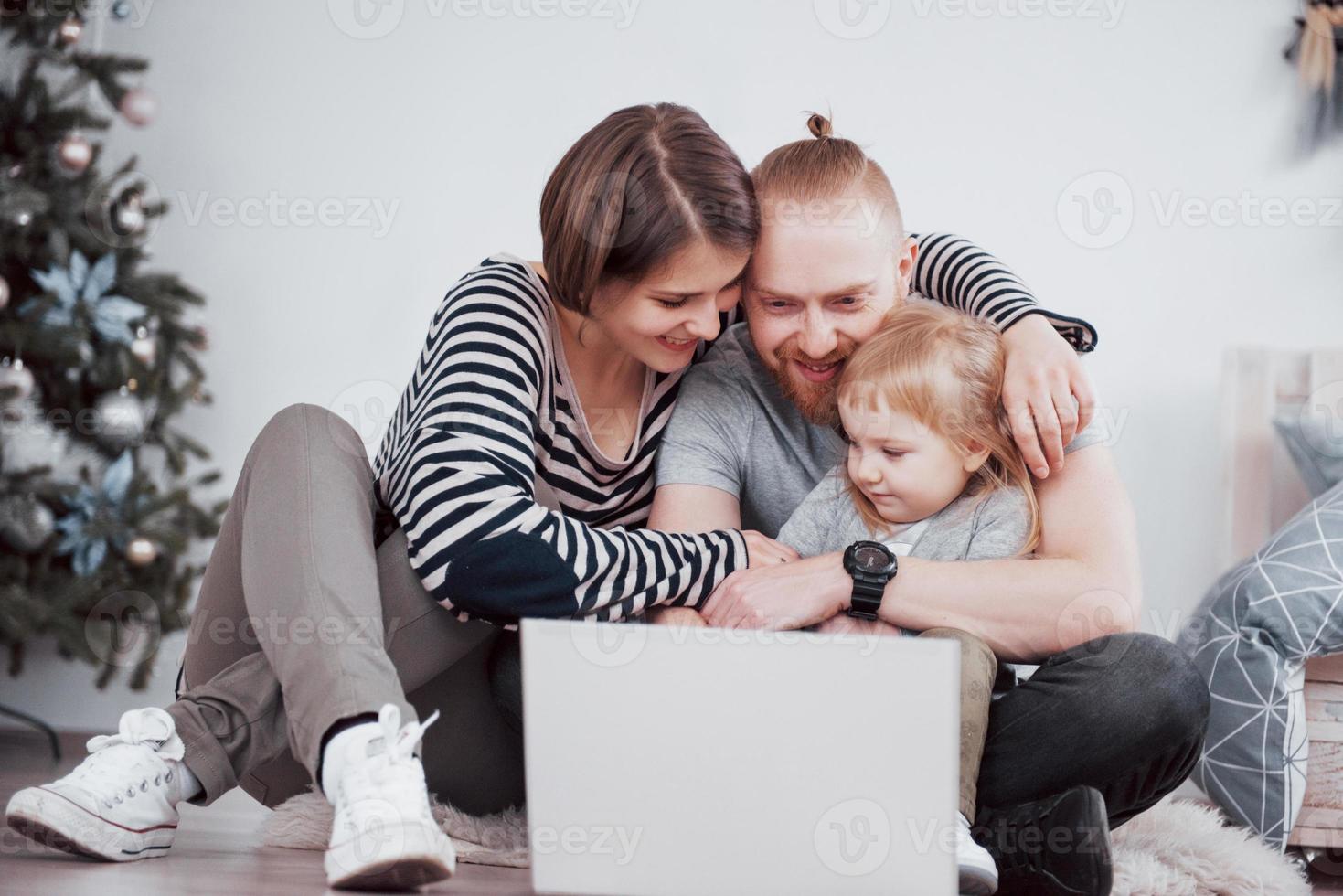 junge dreiköpfige Familie mit Laptop, während sie zu Hause auf dem Teppich liegt foto