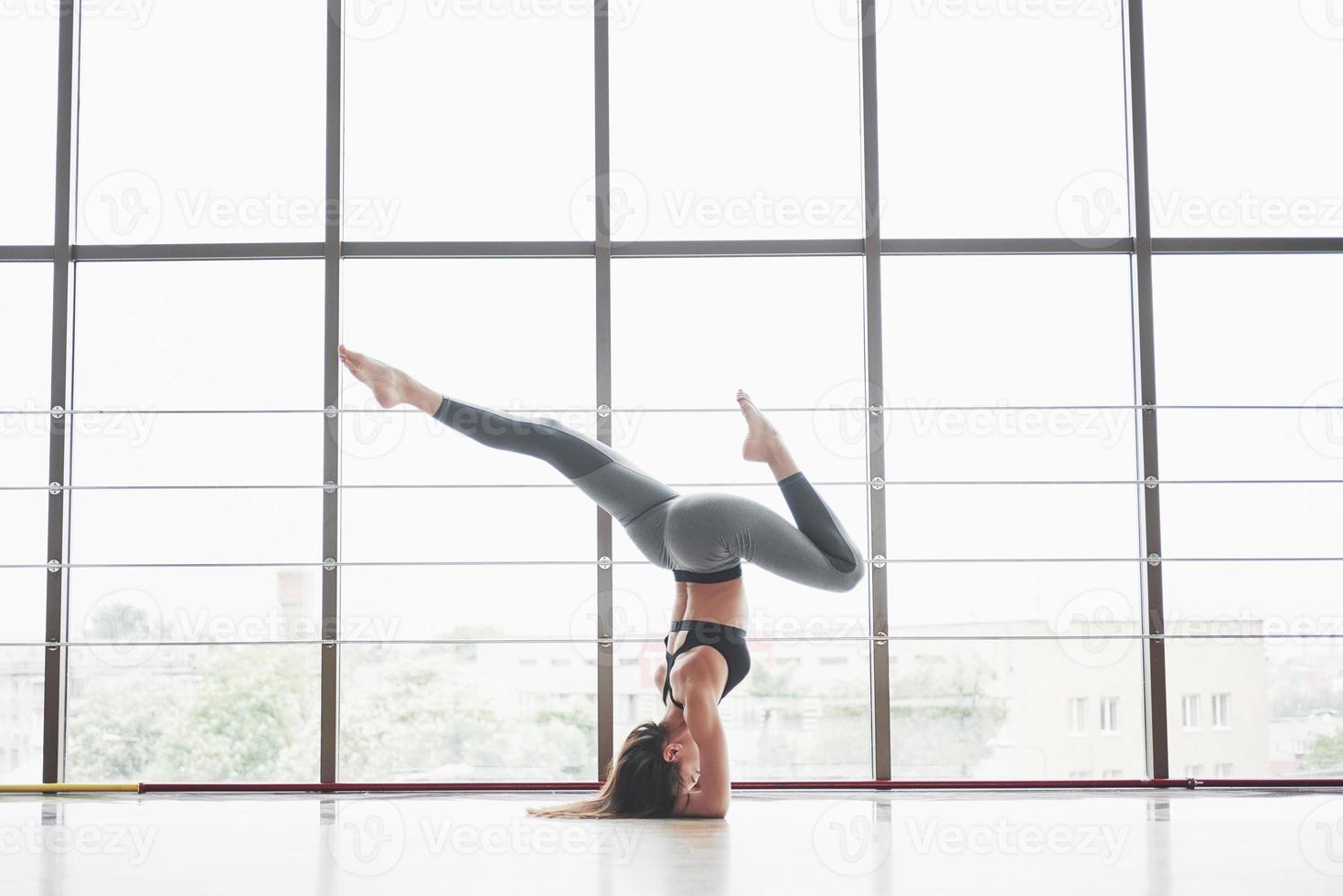 eine Sportfrau, die Yogastunden macht und ihre Beine in der Nähe des großen Fensters ausstreckt foto