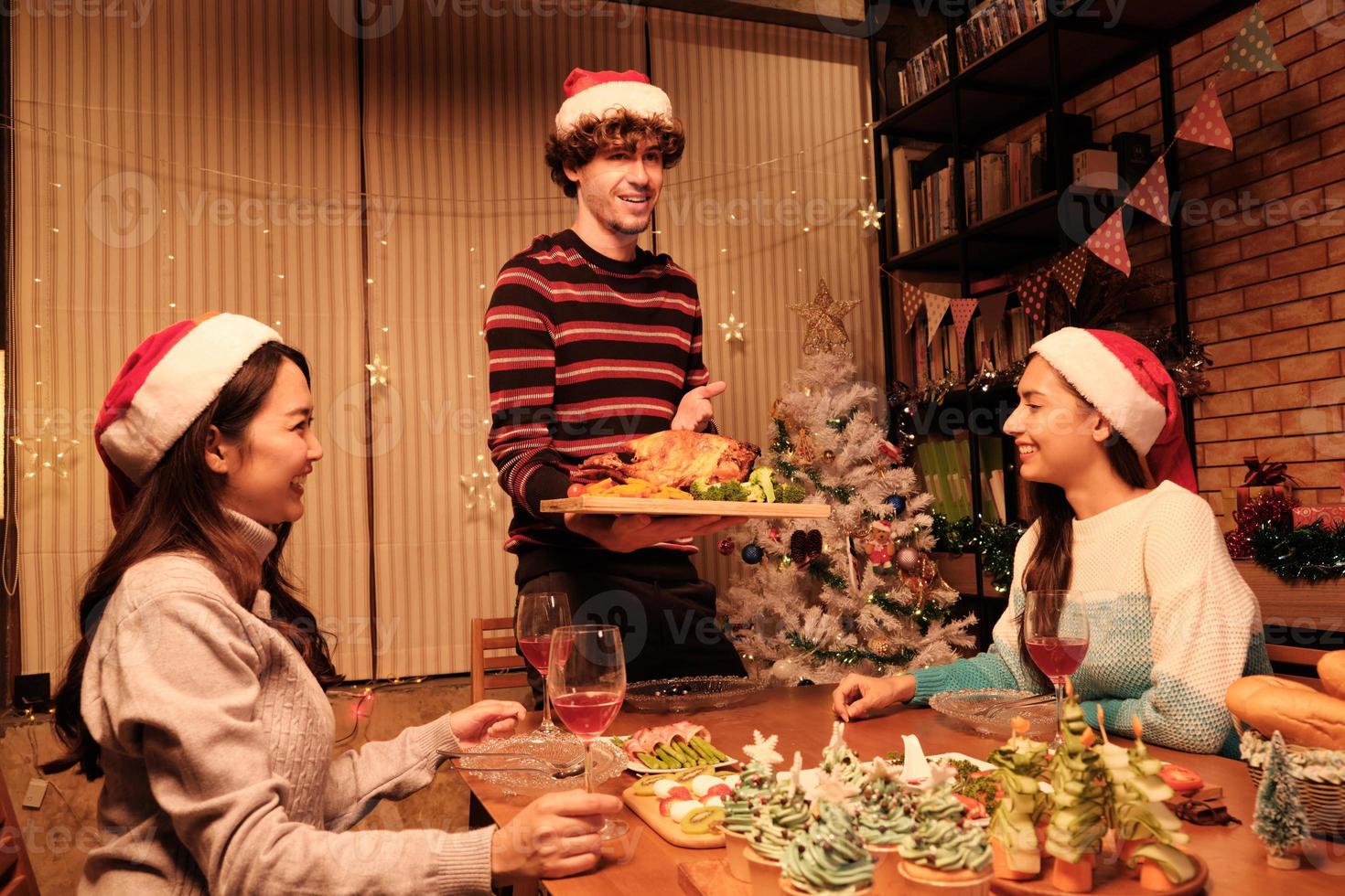 Das besondere Essen der Familie, junger Mann serviert gebratenen Truthahn an Freunde, fröhlich mit Getränken und genießt das Essen, Abendessen im Esszimmer des Hauses, das für Weihnachtsfeste und Neujahrsfeiern dekoriert ist. foto