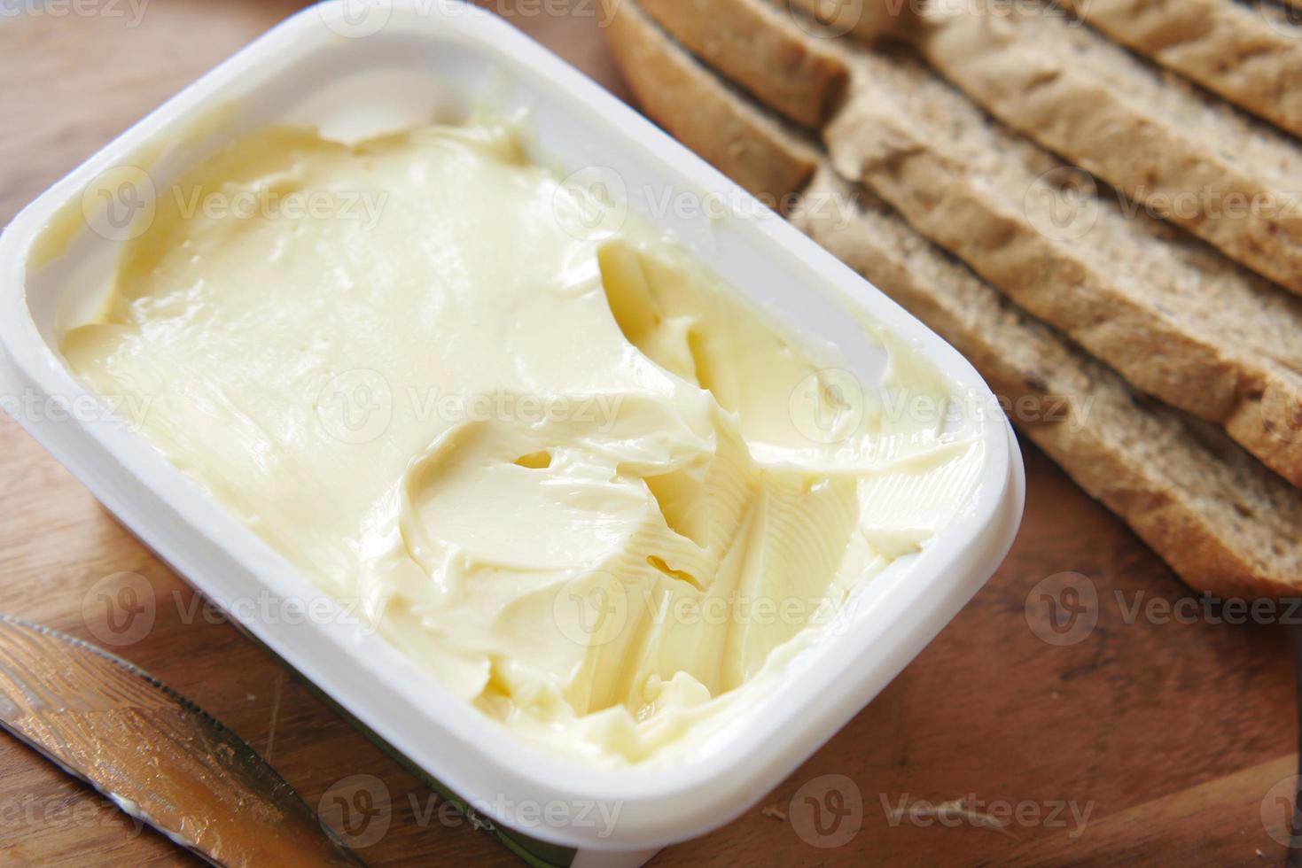gesalzene Butter in einem Plastikbehälter und Brot auf dem Tisch foto