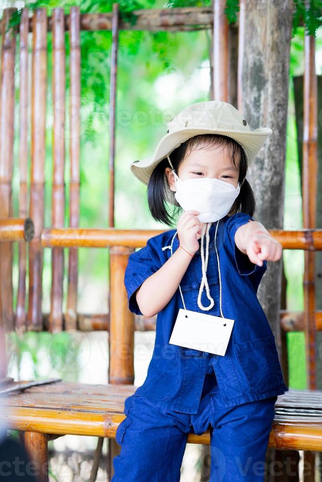 Ein süßes Mädchen trägt eine weiße chirurgische Gesichtsmaske, um die Ausbreitung des Virus und kleinen giftigen Staubs zu verhindern pm2.5. Kind zeigt mit dem Finger nach vorne und beantwortet selbstbewusst Fragen. foto