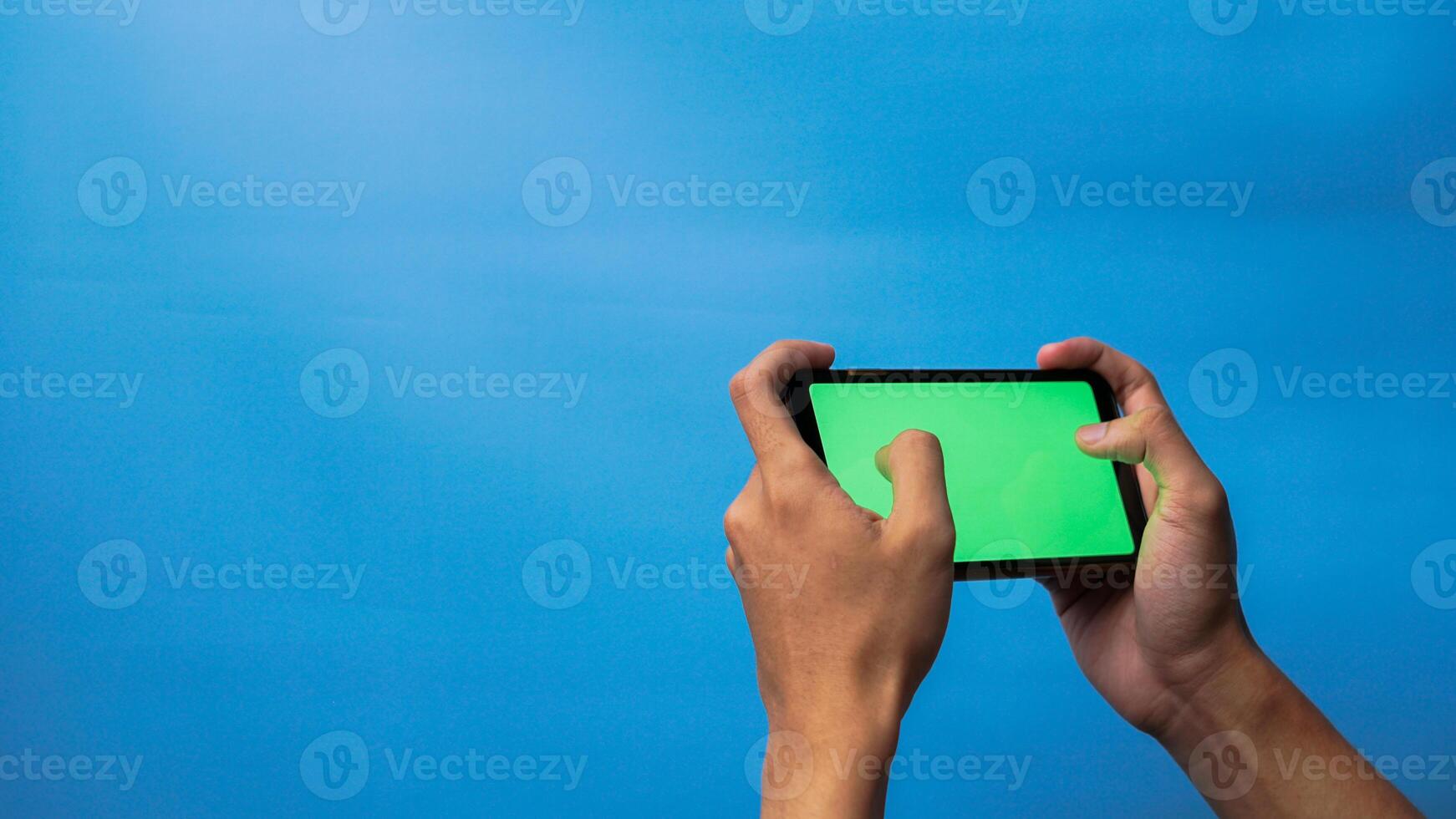 Hand von Mann halten Handy, Mobiltelefon Smartphone Grün Bildschirm mit Spiel spielen Geste auf Blau Hintergrund foto
