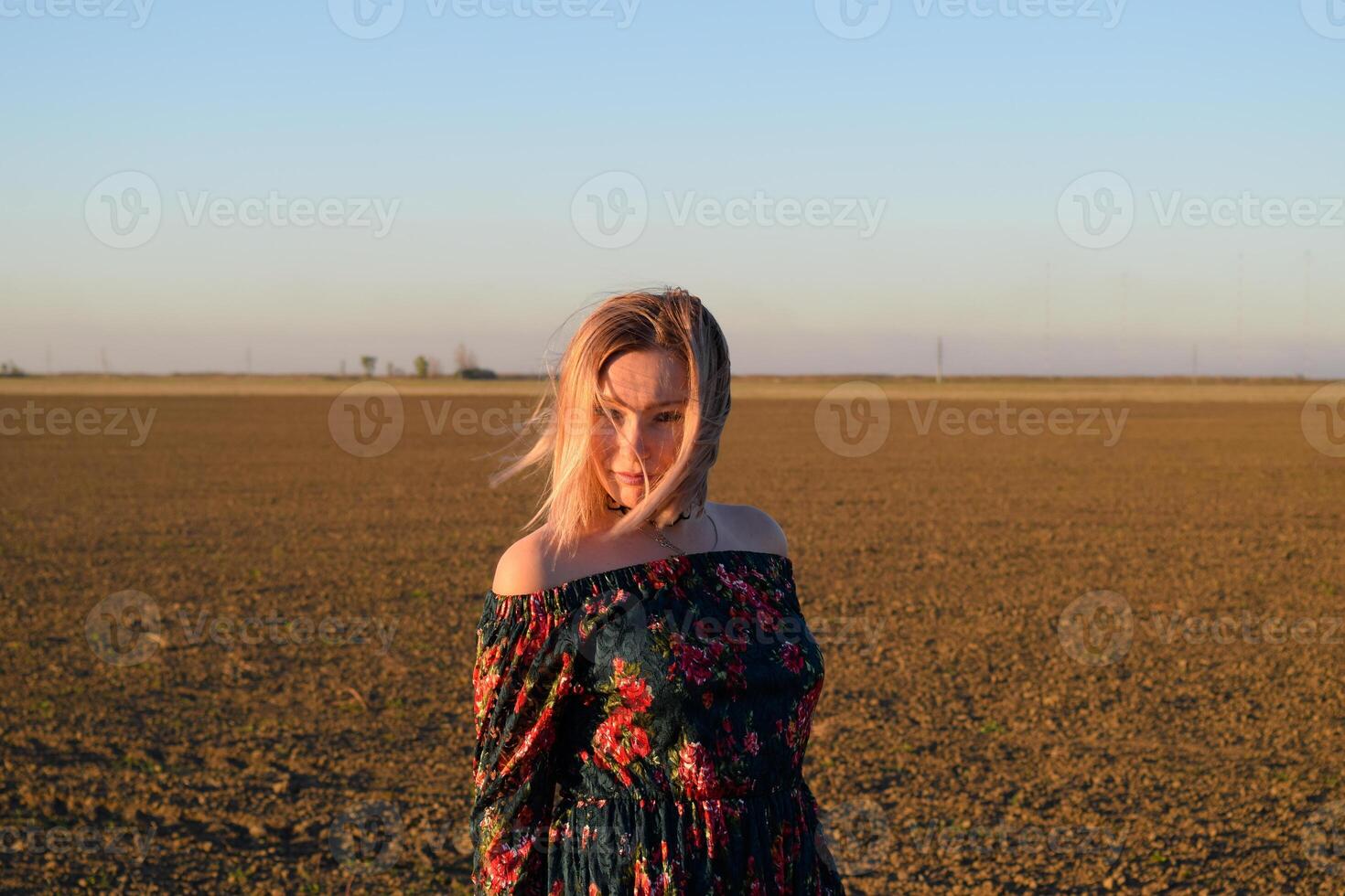 Frau im ein gepflügt Feld im ein rot schwarz Kleid auf ein Sonnenuntergang Hintergrund. foto