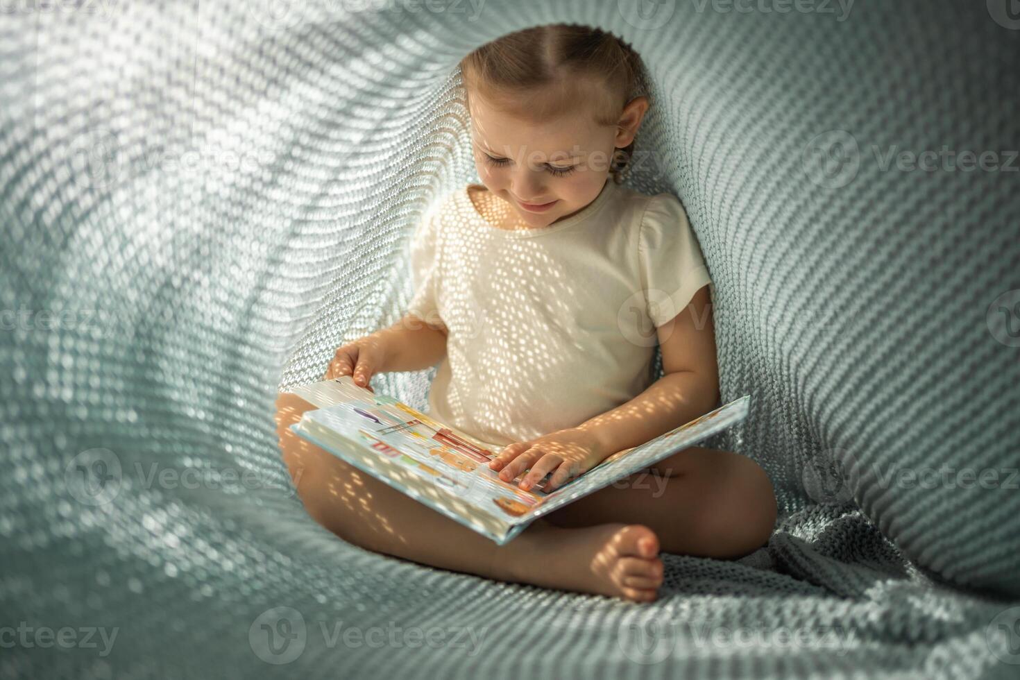 wenig Mädchen genießen von Rezension ein Buch unter Blau gestrickt Plaid im sonnig Morgen foto