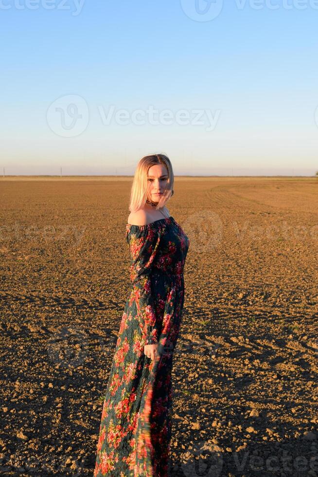 Frau im ein gepflügt Feld im ein rot schwarz Kleid auf ein Sonnenuntergang Hintergrund. foto