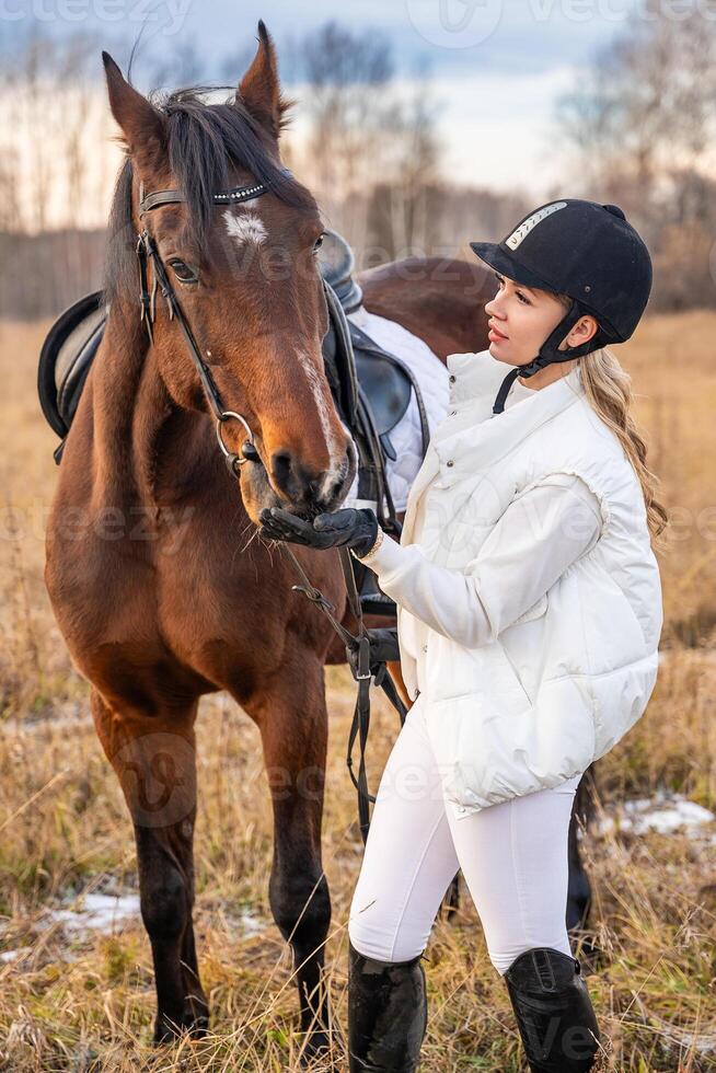 blond Fachmann weiblich Jockey Stehen in der Nähe von Pferd im Feld. Freundschaft mit Pferd. hoch Qualität Foto