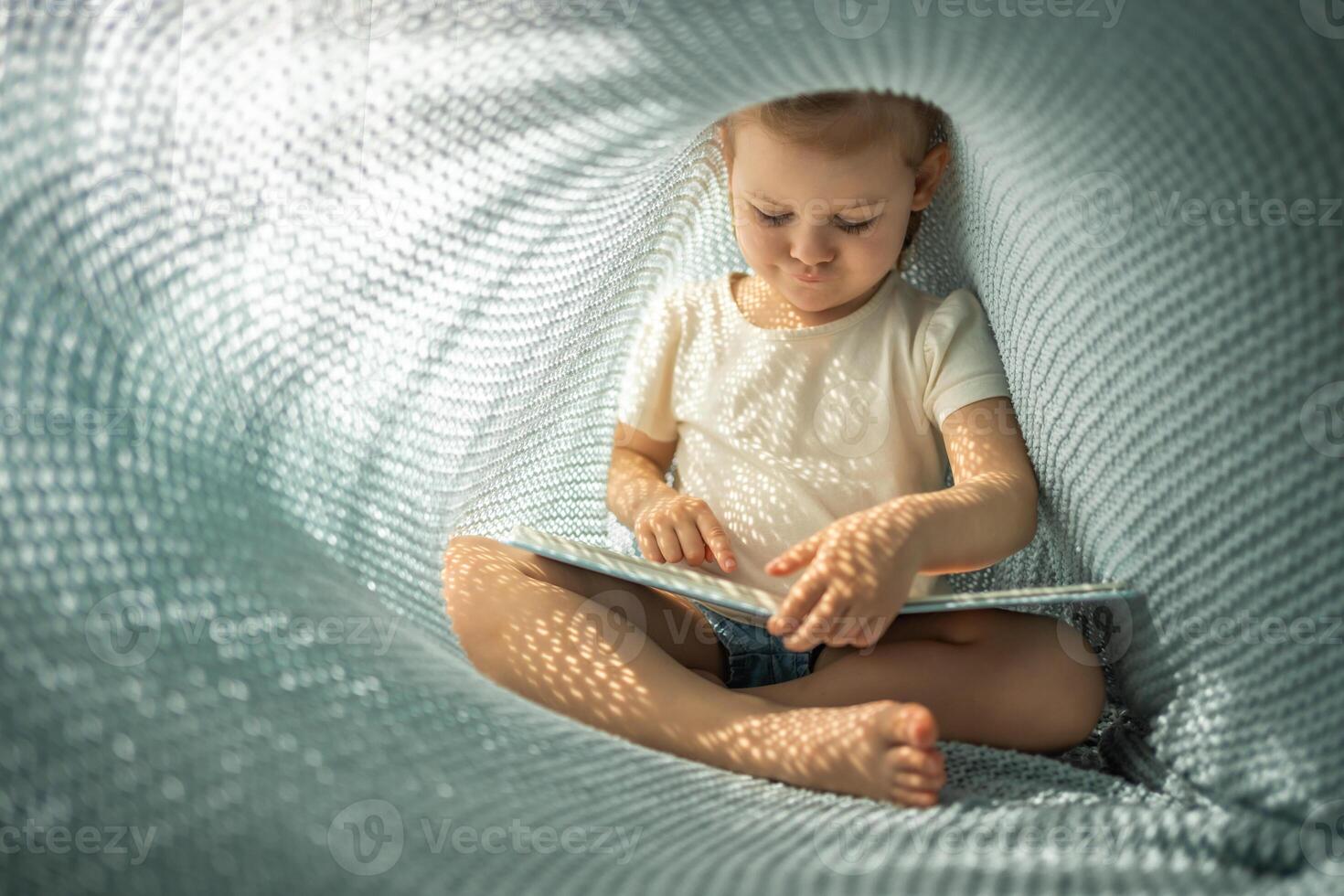 wenig Mädchen genießen von Rezension ein Buch unter Blau gestrickt Plaid im sonnig Morgen foto