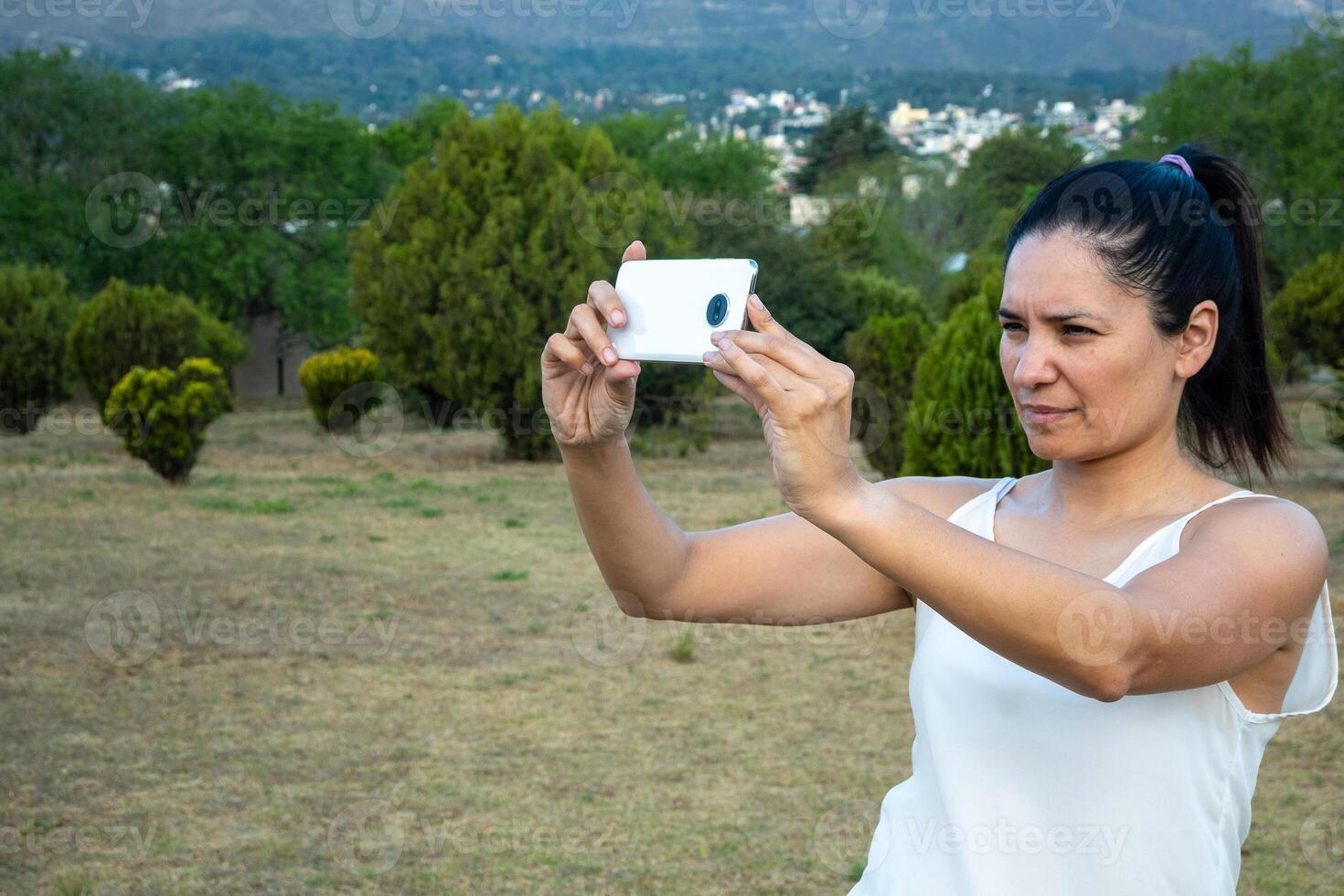 Latein Frau mit ihr Zelle Telefon im ein Park. foto