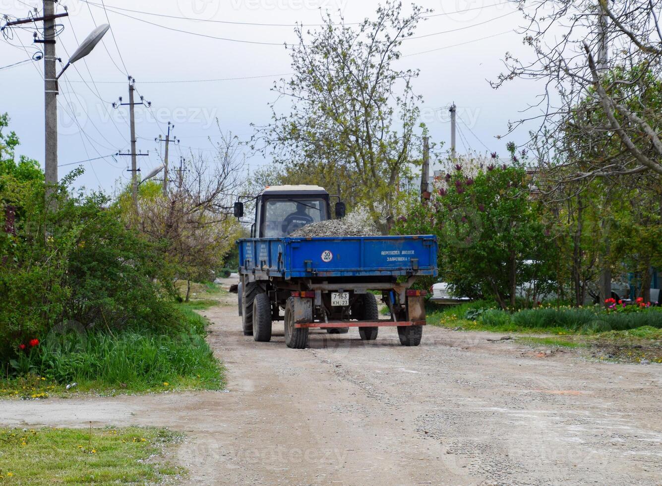 Traktor mit ein Schutt Wagen zum reparieren das Straße. Fütterung Löcher auf das Straße. Straße Reparatur. foto