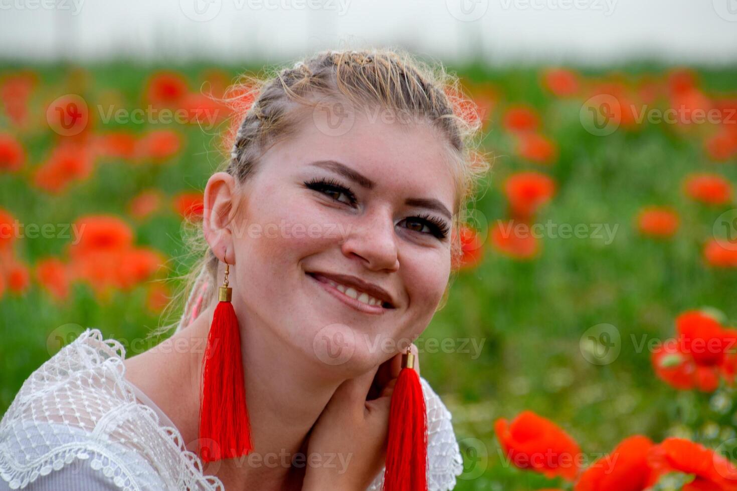 blond jung Frau im rot Rock und Weiß Shirt, rot Ohrringe ist im das Mitte von ein Mohn Feld. foto