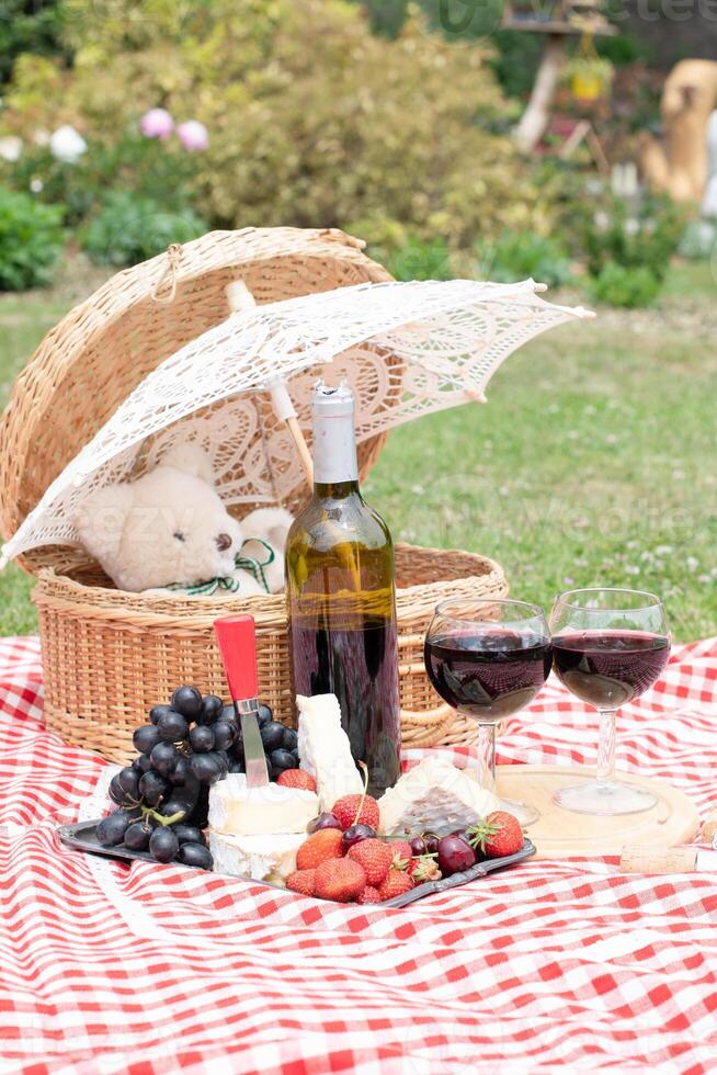 Sommer- Picknick auf ein Grün Rasen mit rot Wein, Käse und frisch Beeren, Trauben foto