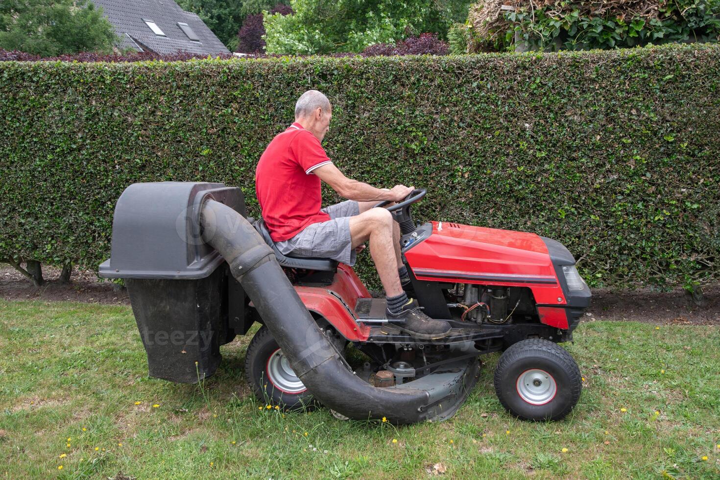 Rasen Mäher mäht das Gras, ein mittleren Alters männlich Gärtner funktioniert auf ein Mini Traktor foto