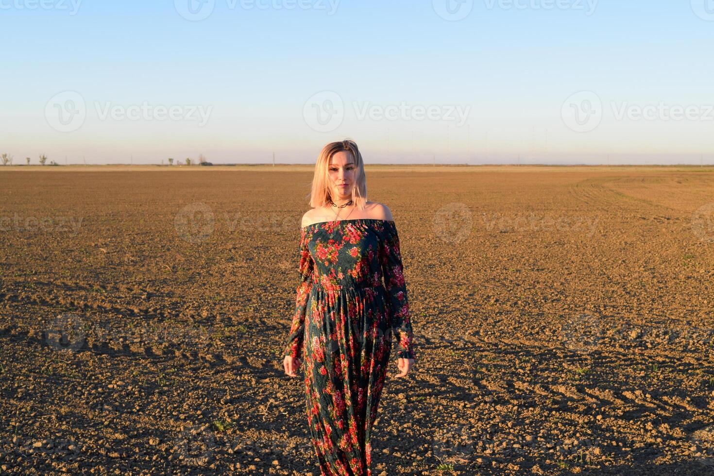 Frau im ein gepflügt Feld im ein rot schwarz Kleid auf ein Sonnenuntergang Hintergrund. foto