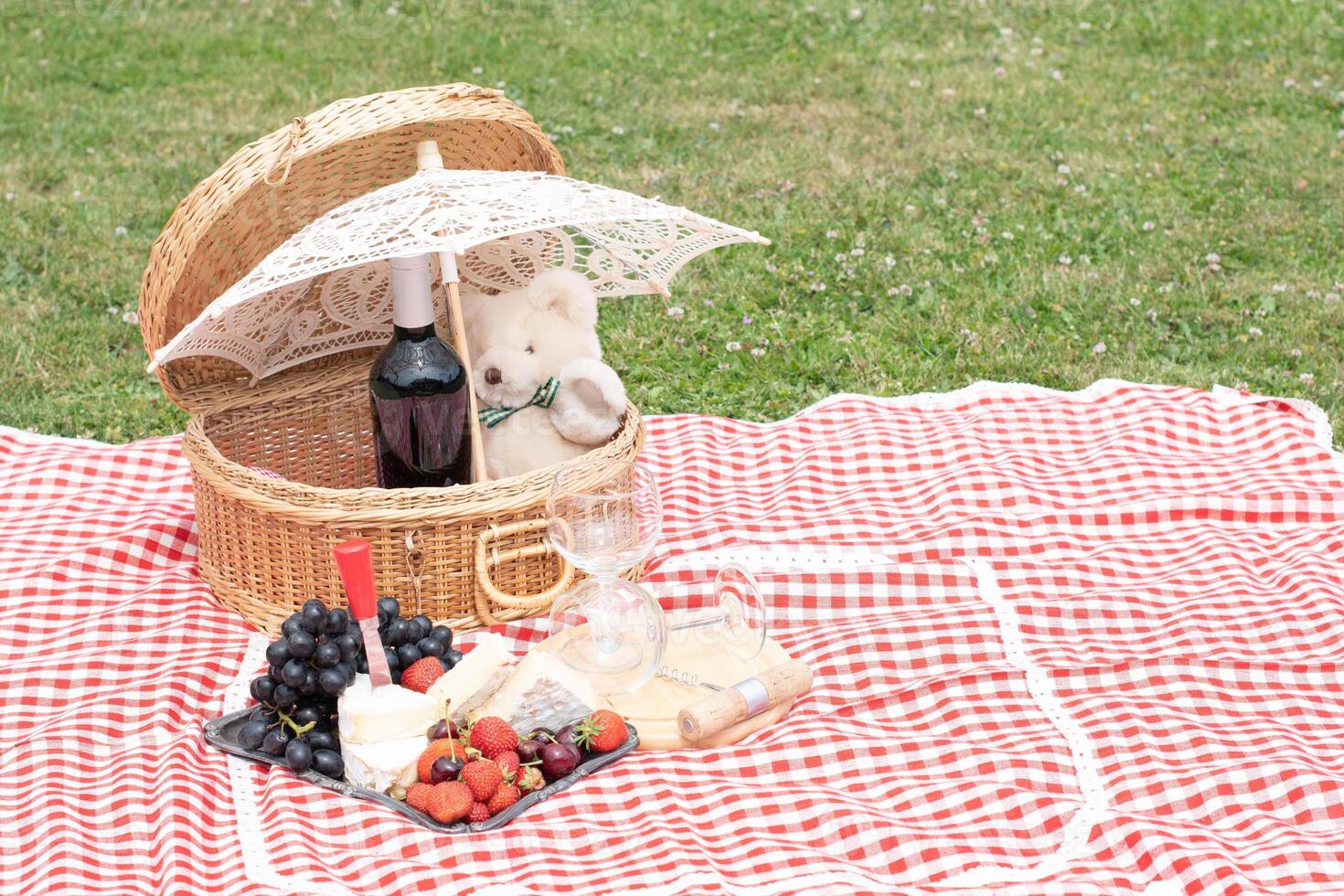 Sommer- Picknick auf ein Grün Rasen mit rot Wein, Käse und frisch Beeren, Trauben foto
