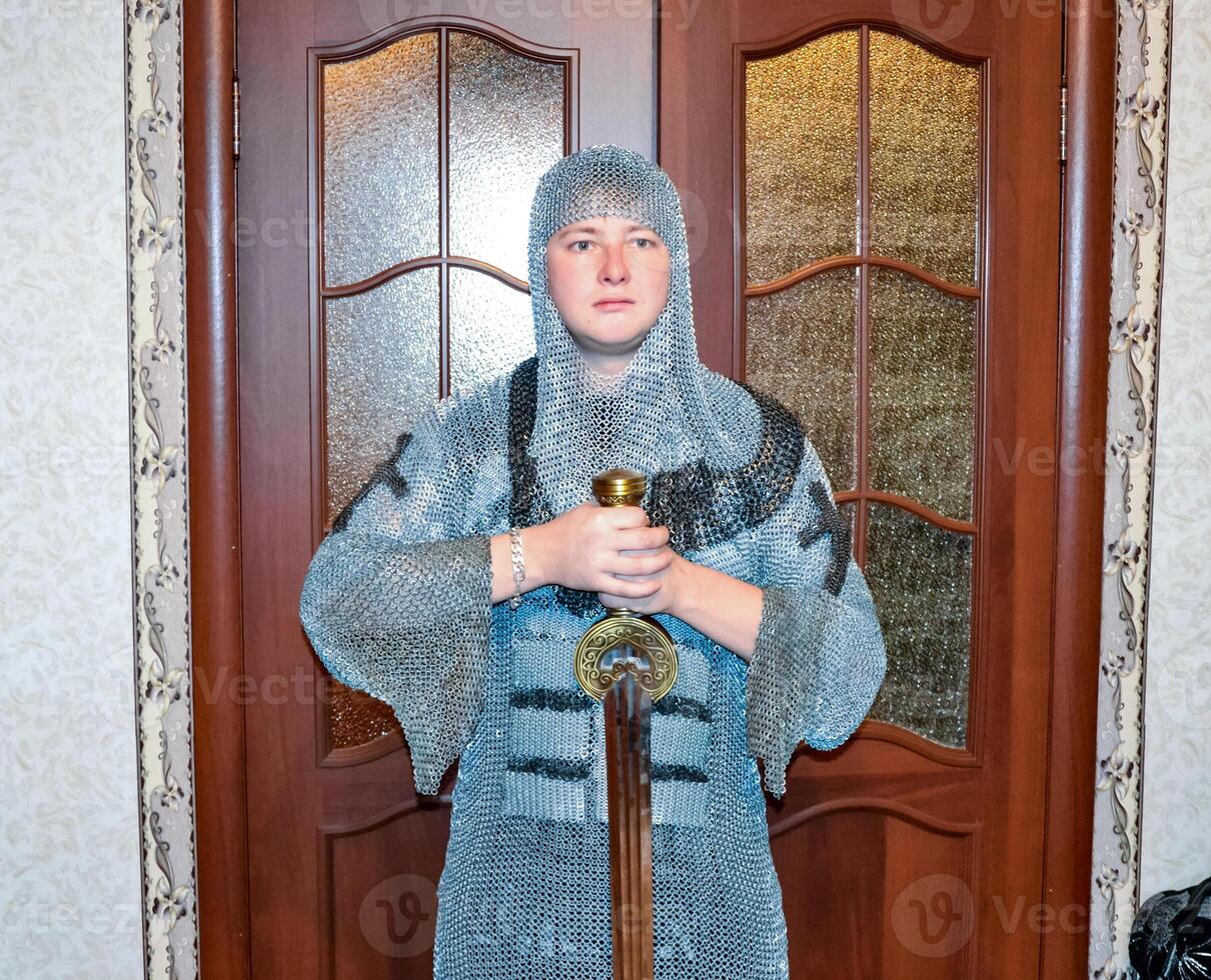 ein Mann gekleidet oben im ein Ritter- Halsberge beim Zuhause im seine Zimmer. Ritter- Schwert im das Hände von ein Mann. foto