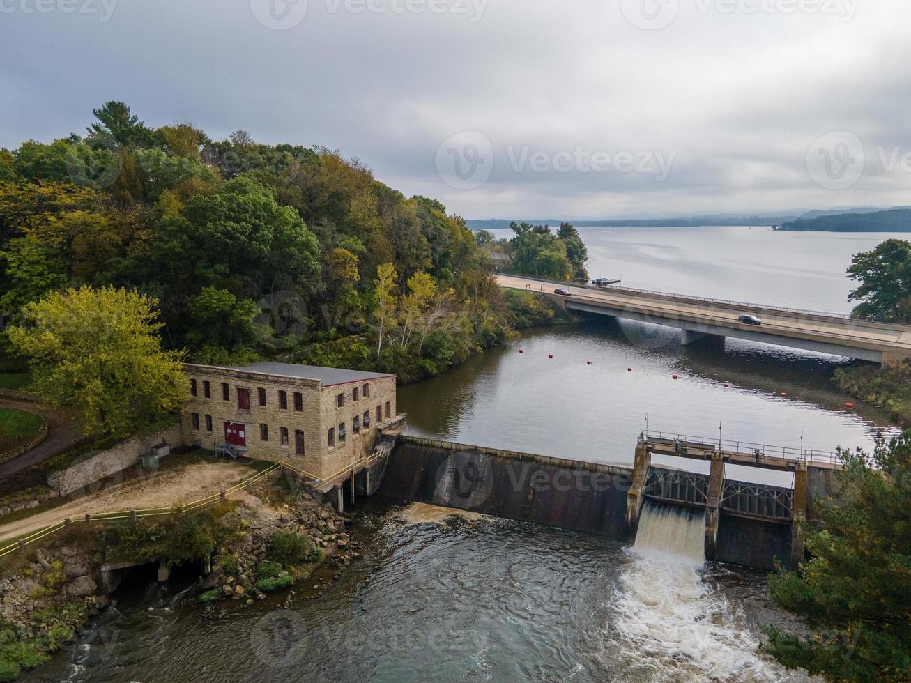 Luftaufnahme des Damms mit Brücke über den Fluss zum See im Herbst historisches Steuerhaus mit Schotterstraße aktiver Überlauf foto