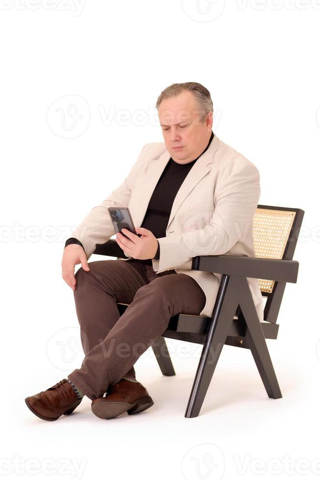 Mann im ein Stuhl Aufpassen etwas auf seine Telefon auf ein Weiß Hintergrund foto