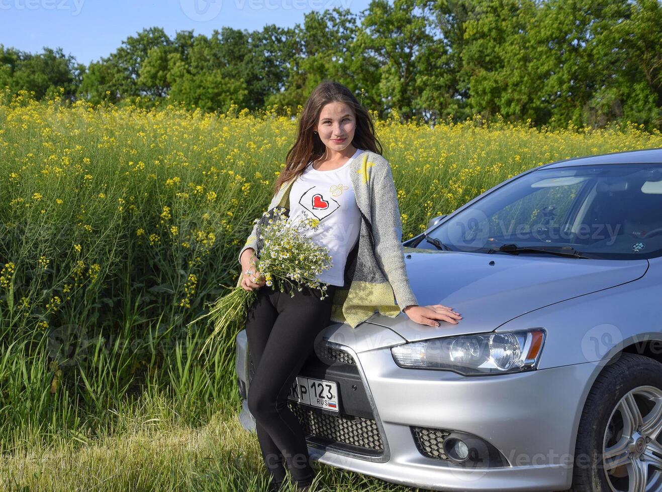 ein schön jung Frau mit ein Strauß von Gänseblümchen steht in der Nähe von ein Silber Auto foto