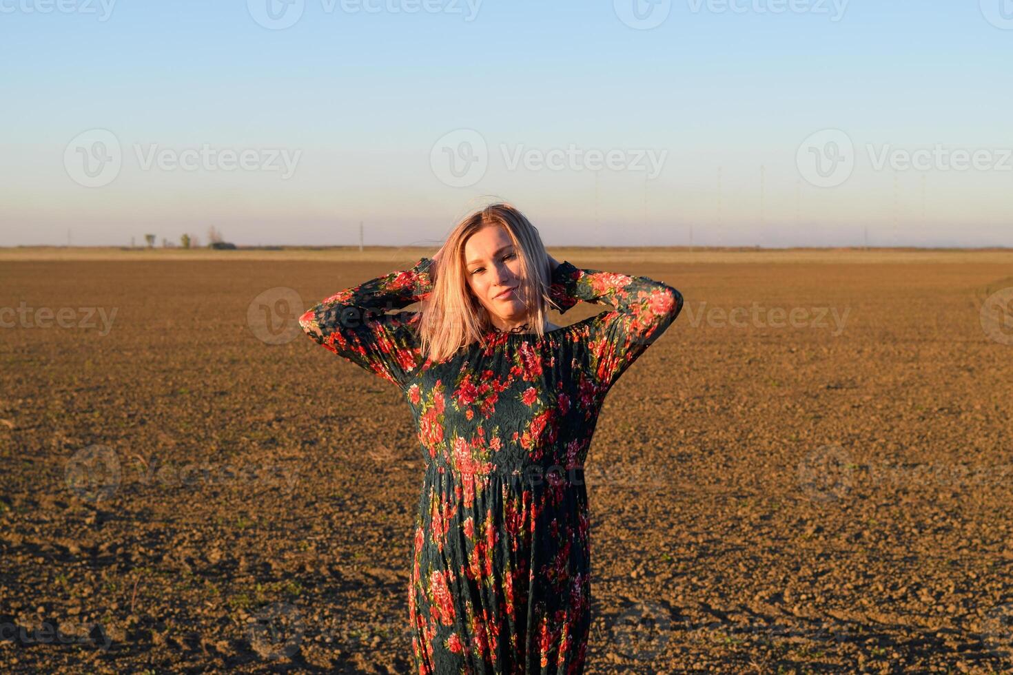 Frau im ein gepflügt Feld im ein rot schwarz Kleid auf ein Sonnenuntergang Hintergrund. foto