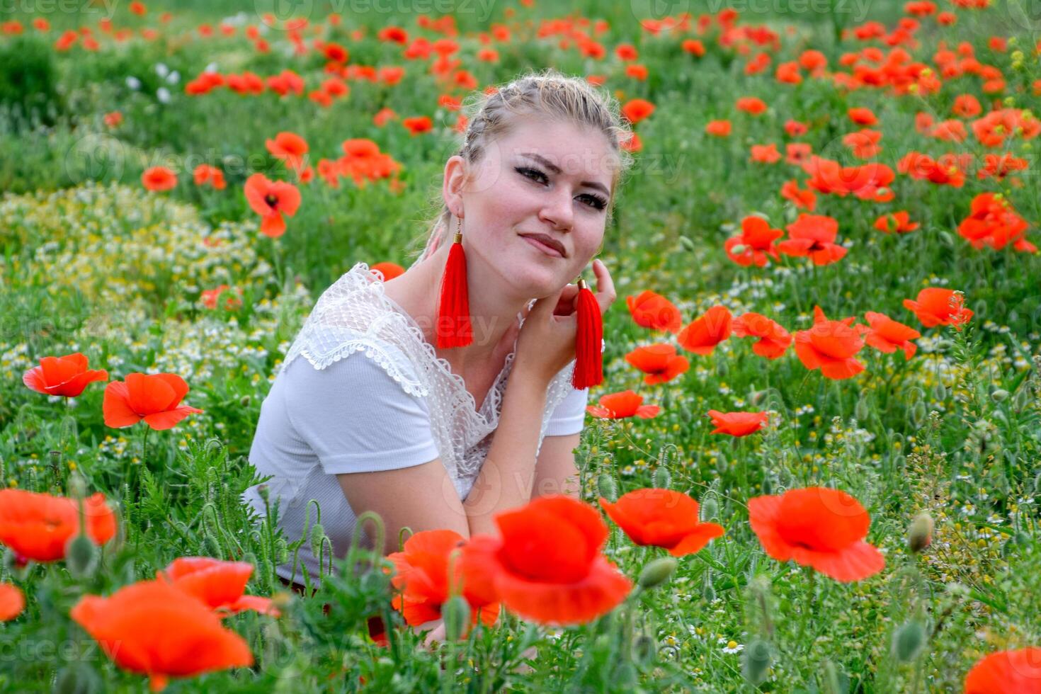 blond jung Frau im rot Rock und Weiß Shirt, rot Ohrringe ist im das Mitte von ein Mohn Feld. foto