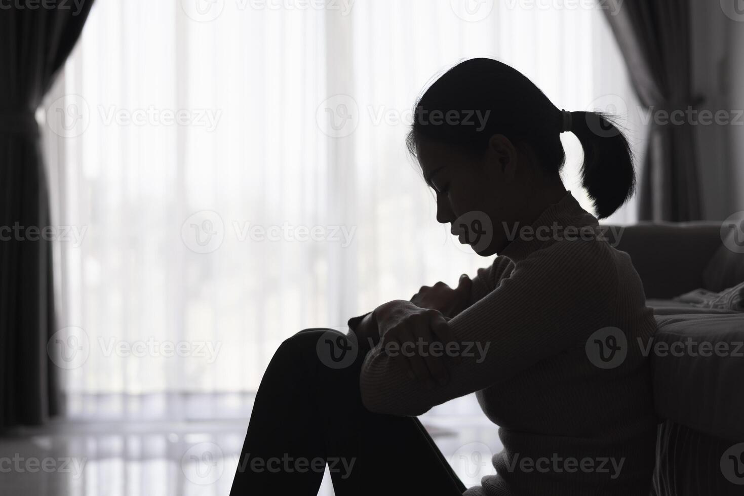 Silhouette von ein Person Leiden von Depression im das Haus, deprimiert Frau Sitzung allein auf das Sofa Gefühl betonen, traurig und besorgt im das dunkel Zimmer. Person sind betont. foto