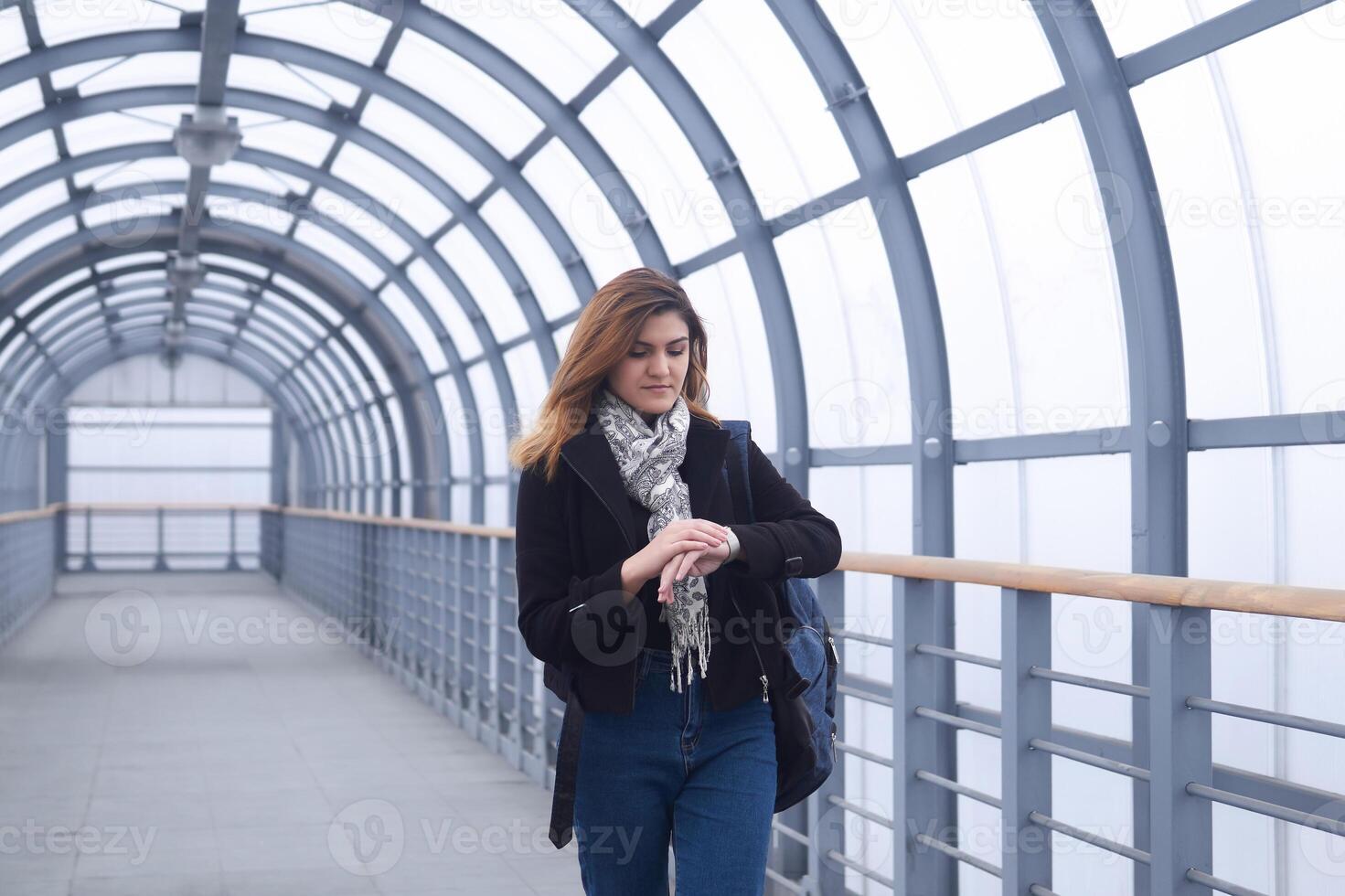 jung Frau Spaziergänge entlang ein bedeckt Gehweg und sieht aus beim ihr Uhr foto