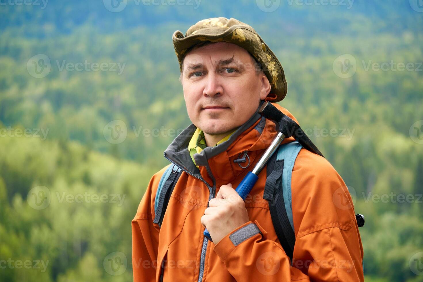 Porträt von ein Mann Geologe mit ein Rucksack und ein geologisch Hammer gegen das bewaldet Berg Landschaft foto