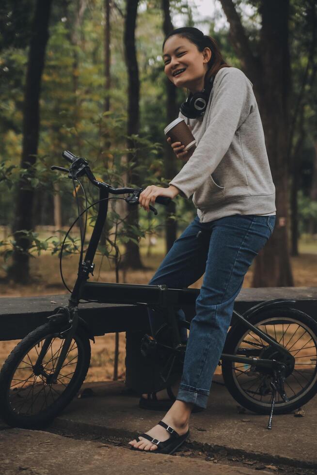 glücklich asiatisch jung Frau gehen und Reiten Fahrrad im Park, Straße Stadt ihr lächelnd mit Fahrrad von Transport, Öko freundlich, Menschen Lebensstil Konzept. foto
