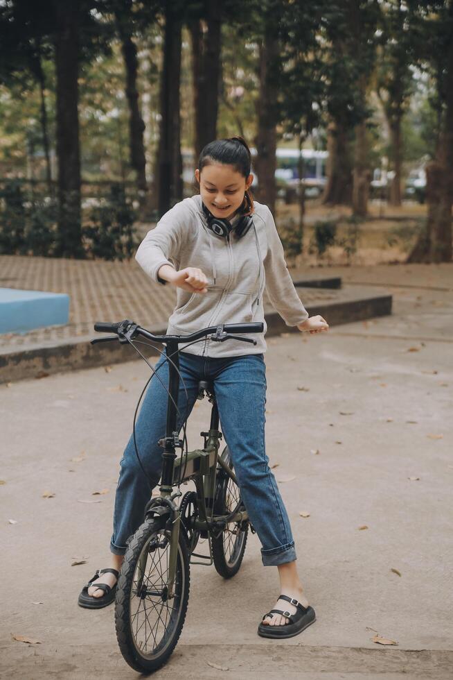 glücklich asiatisch jung Frau gehen und Reiten Fahrrad im Park, Straße Stadt ihr lächelnd mit Fahrrad von Transport, Öko freundlich, Menschen Lebensstil Konzept. foto