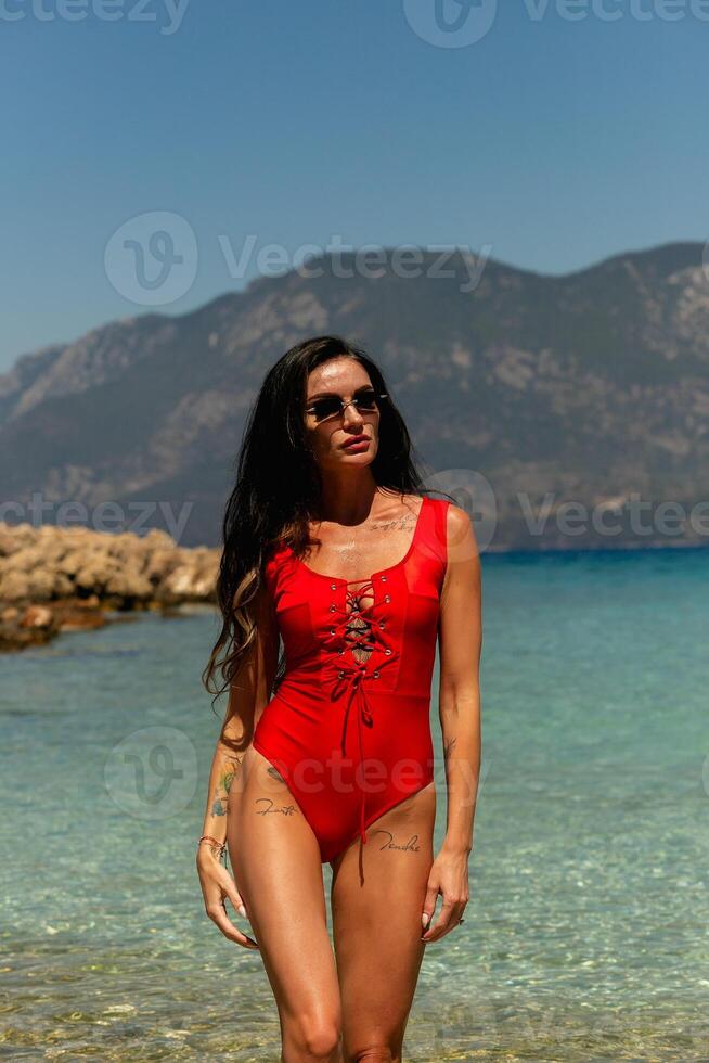 schön jung Frau im ein rot Badeanzug Stehen beim Meer Strand foto