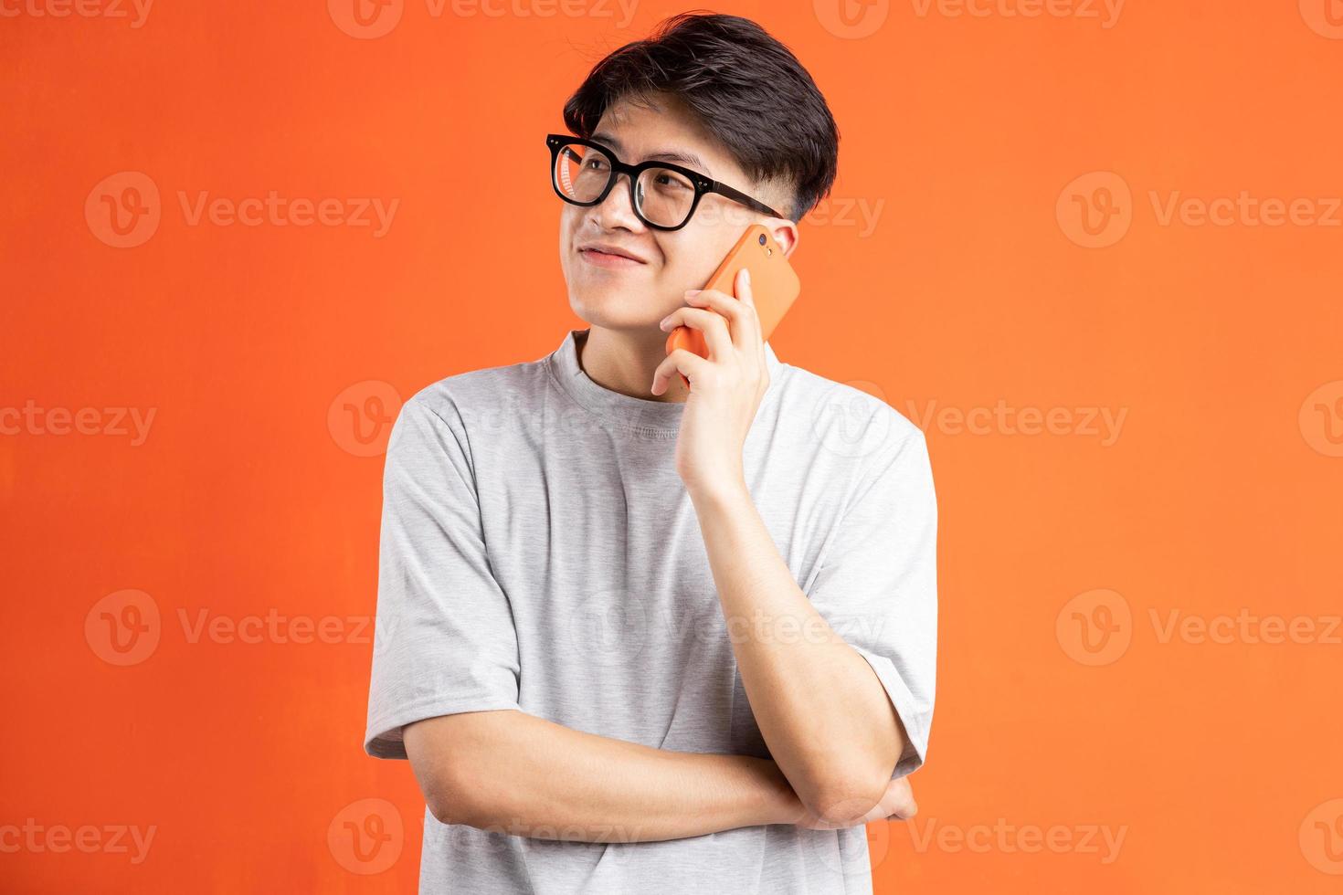 Porträt eines jungen asiatischen Mannes am Telefon, isoliert auf orangem Hintergrund foto