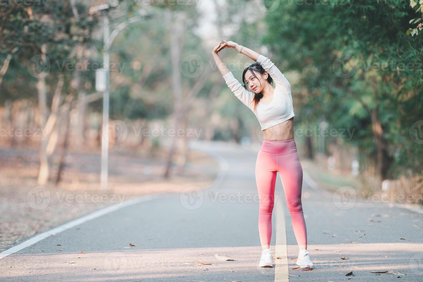 Fitness Konzept, aktiv Frau im Sportbekleidung tun ein Seite strecken auf ein ruhig Straße inmitten Natur, Fokussierung auf ihr Fitness. foto