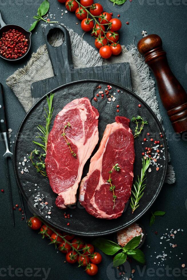 zwei roh Rippe Auge Rindfleisch Steaks mit Gewürze auf ein Platte. bereit zu kochen. auf ein dunkel Stein Hintergrund. oben Sicht. foto