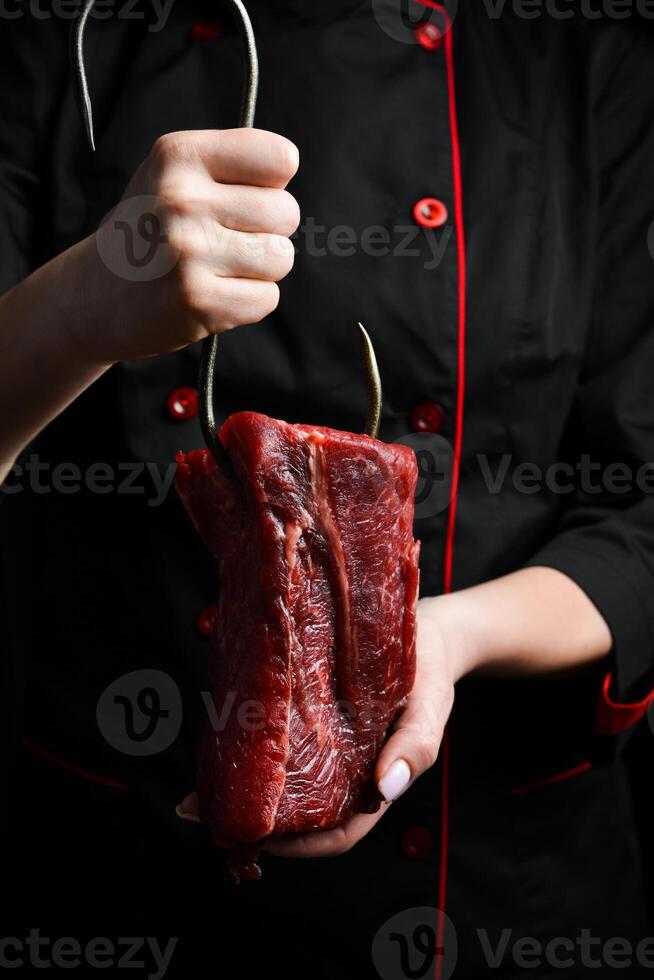 ein Metzger hält ein Stück von Kalbfleisch auf ein Metall Haken. Fleisch Vorbereitung. auf ein schwarz Hintergrund. foto