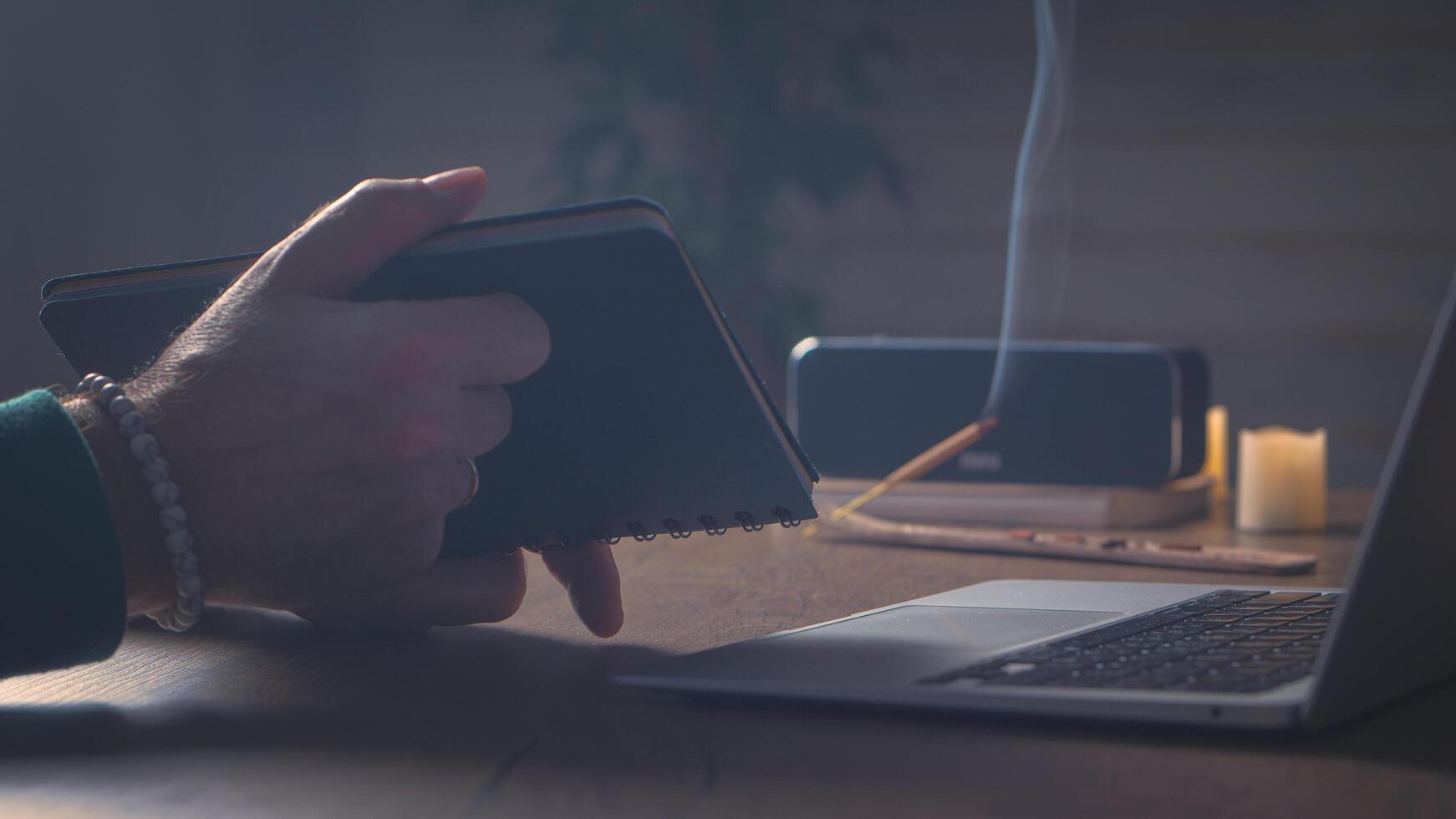 Zuhause Büro. Laptop, Notizblock, Musik- Lautsprecher, Weihrauch. ein Mann im ein Grün Pullover. filmisch-5,5k foto