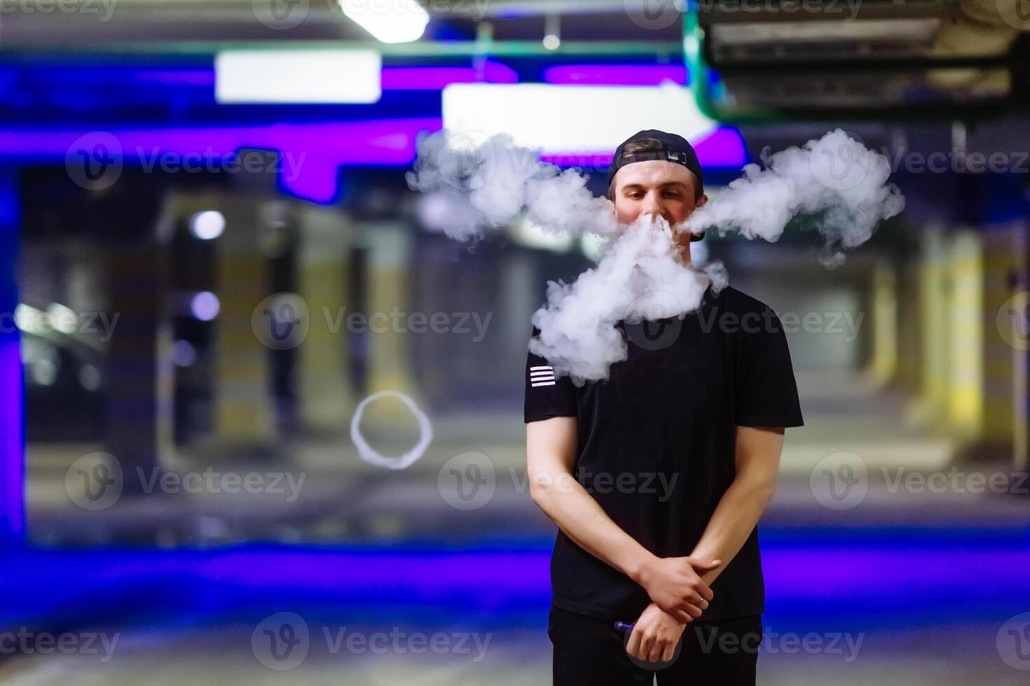 Mann im Deckel Rauch ein elektronisch Zigarette und Veröffentlichungen Wolken von Dampf durchführen verschiedene nett von vaping Tricks foto