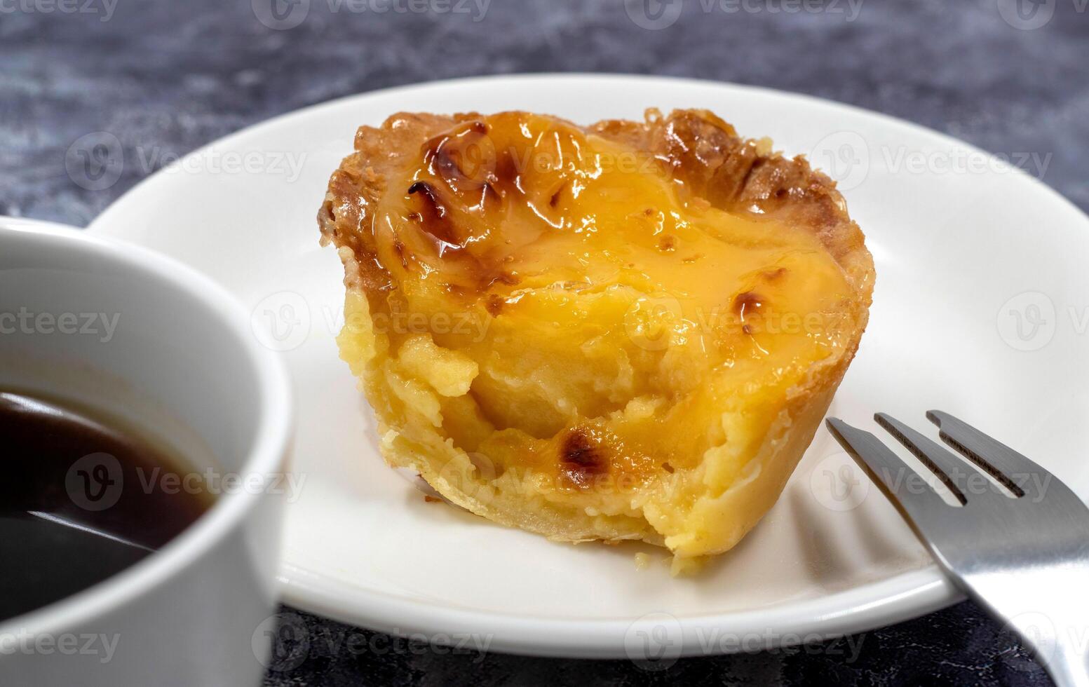 einer nicht gefressen Pastell- de nata oder Portugiesisch Ei Dessert auf ein Weiß Platte. Pastell- de Belm ist ein klein Kuchen mit ein knusprig Puff Gebäck Kruste und ein Pudding Sahne Füllung. Essen ein klein Nachtisch, ein Cupcake. foto