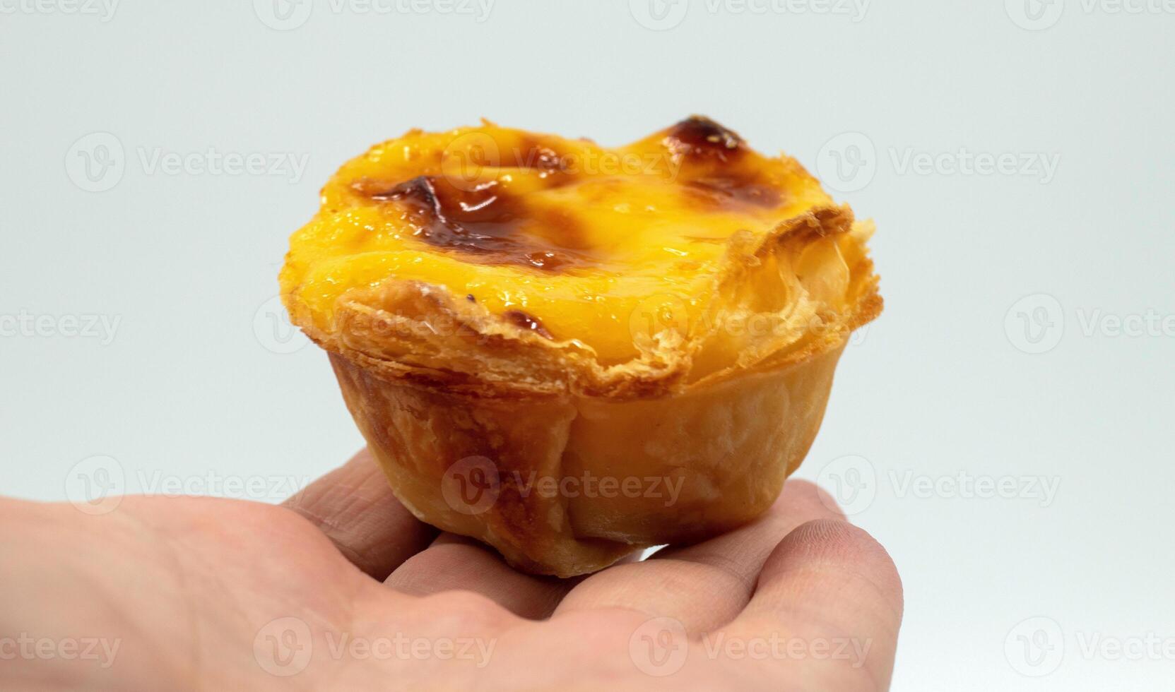 ein des Mannes Hand hält einer Portugiesisch Pastell- de nata Kuchen mit Pudding und Zimt Stöcke auf ein Weiß Hintergrund. Pastell- de belem ist ein Gebäck mit ein verbrannt oben und ein knusprig Puff Gebäck Kruste. foto