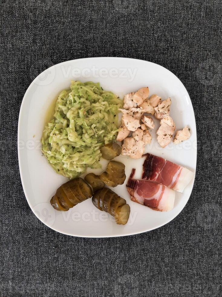 hausgemacht gegrillt Hähnchen mit Zucchini Eintopf, Grün Salat und Gurke Gurken und Schinken serviert auf ein Weiß Teller foto