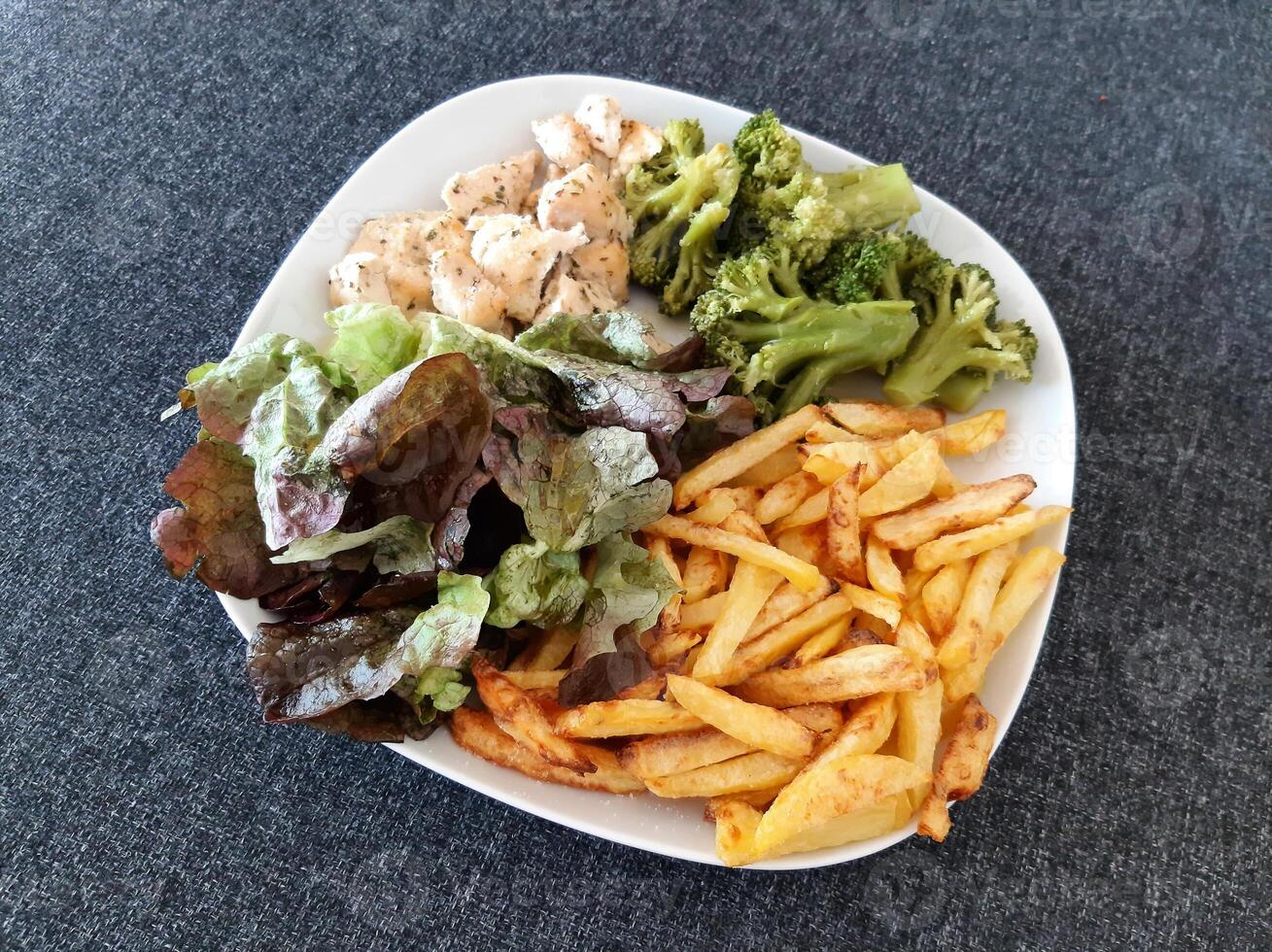 hausgemacht gegrillt Hähnchen mit Französisch Fritten, Brokkoli und Grün Salat, serviert auf ein Weiß Teller foto