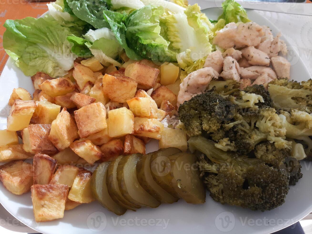 hausgemacht gegrillt Hähnchen mit Französisch Fritten, Grün Salat, Brokkoli und Gurke Gurken serviert auf ein Weiß Teller foto