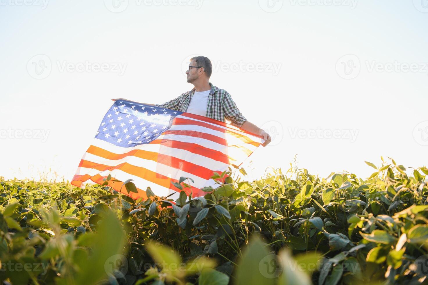 ein jung Farmer steht mit ein USA Flagge im ein Sojabohne Feld. das Konzept von das uns landwirtschaftlich Industrie. foto