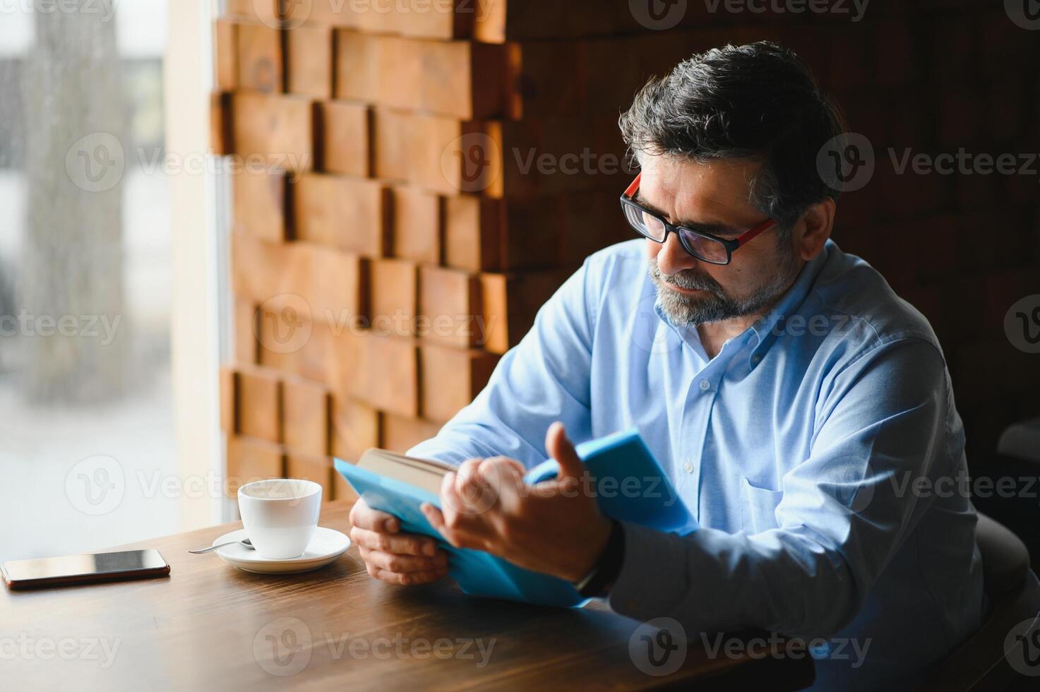 reifen gut aussehend Mann lesen ein Buch im ein Cafe foto