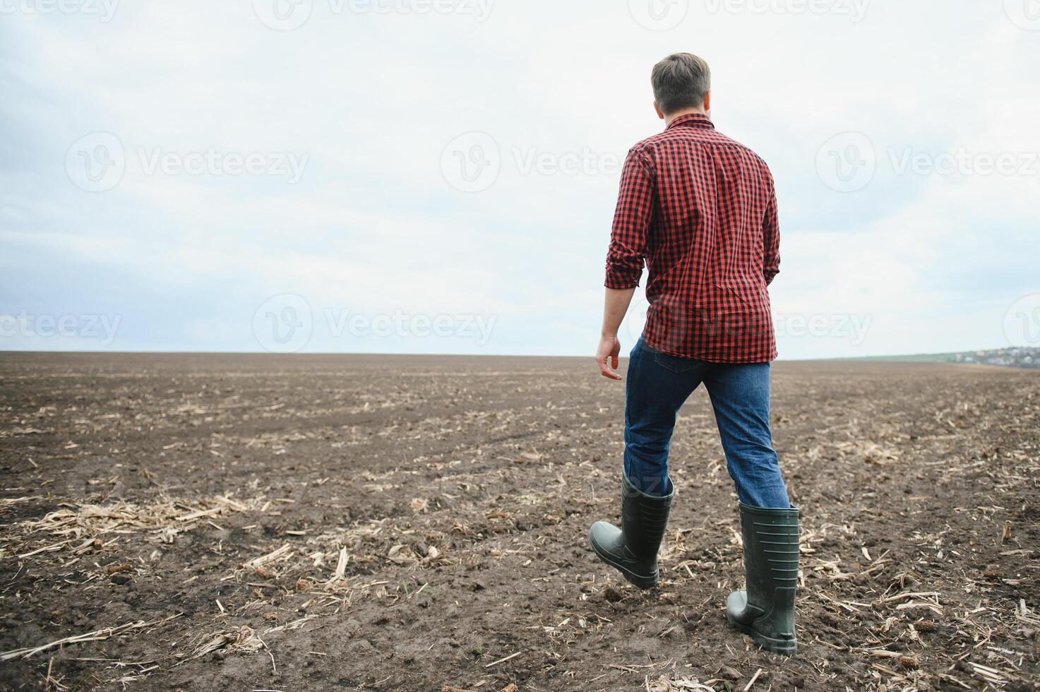 ein Farmer im Stiefel funktioniert mit seine Tablette im ein Feld gesät im Frühling. ein Agronom Spaziergänge das Erde, beurteilen ein gepflügt Feld im Herbst. Landwirtschaft. Clever Landwirtschaft Technologien foto