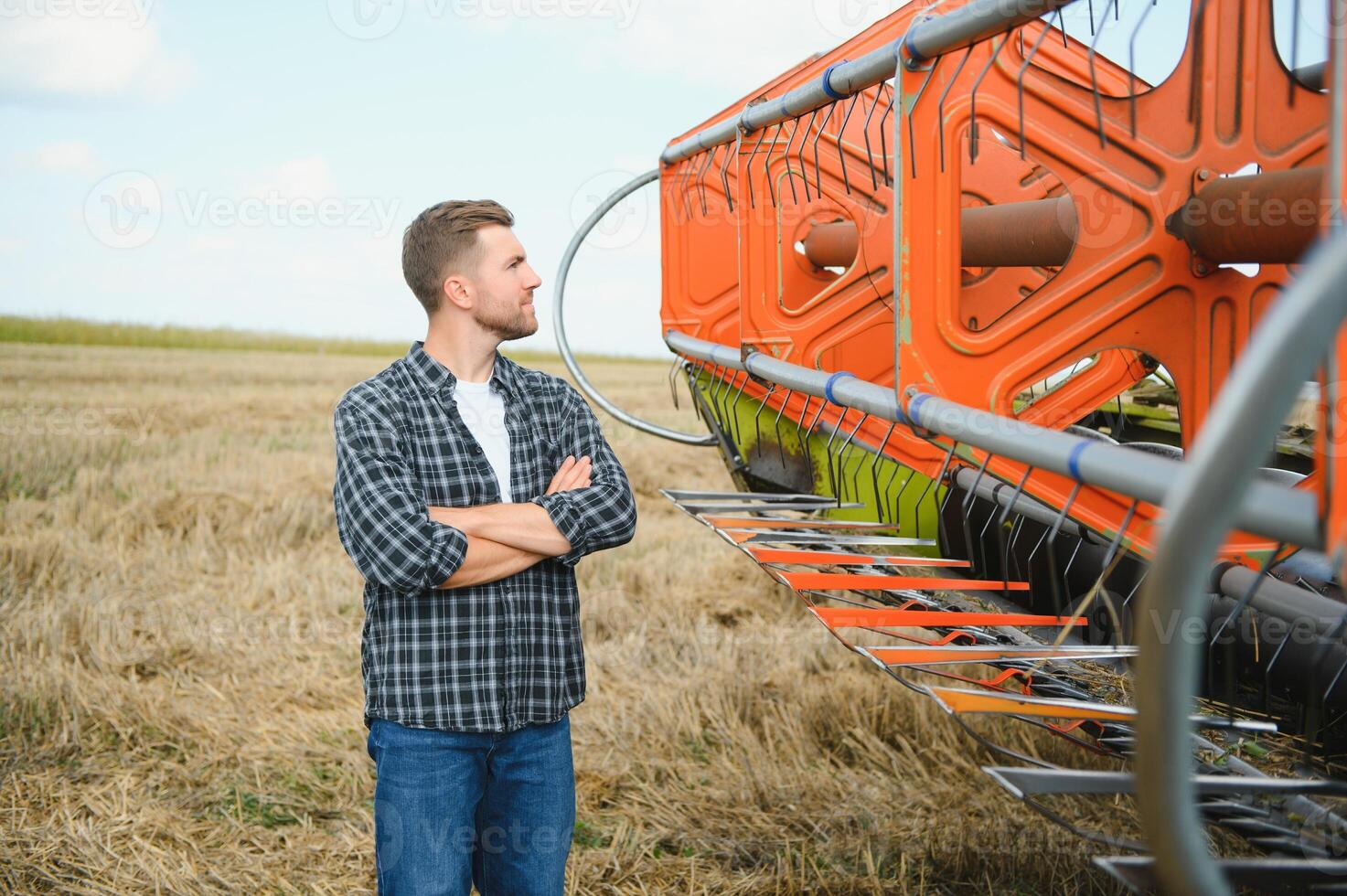 glücklich Farmer stolz Stehen im ein Feld. kombinieren Mähdrescher Treiber gehen zu Ernte Reich Weizen Ernte. Agronom tragen Flanell Shirt, suchen beim Kamera auf ein Ackerland foto