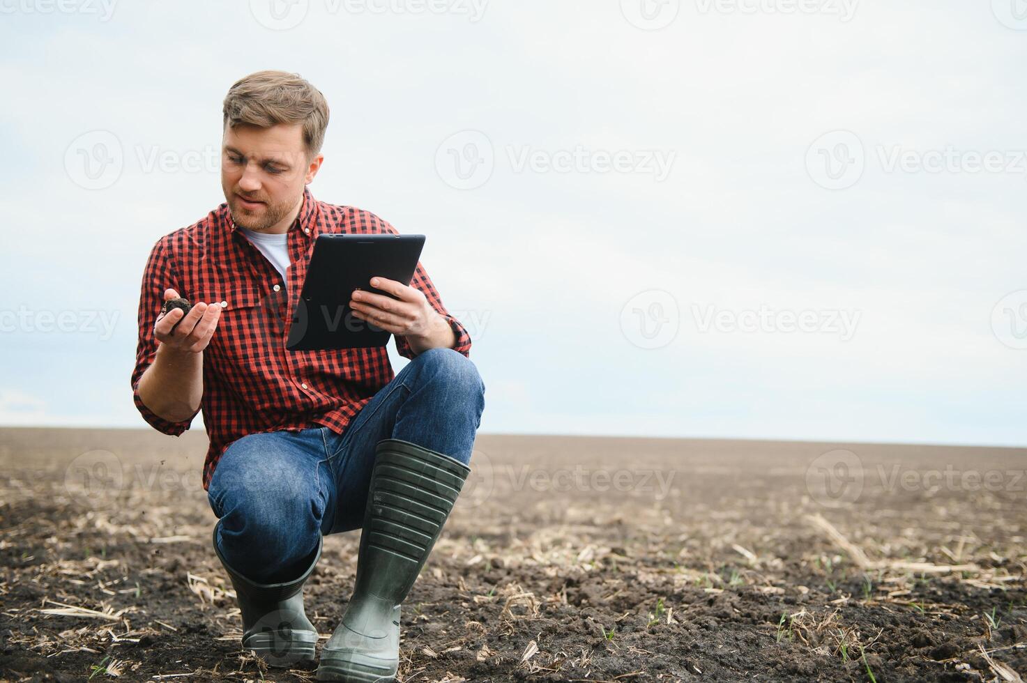 ein Farmer im Stiefel funktioniert mit seine Tablette im ein Feld gesät im Frühling. ein Agronom Spaziergänge das Erde, beurteilen ein gepflügt Feld im Herbst. Landwirtschaft. Clever Landwirtschaft Technologien foto